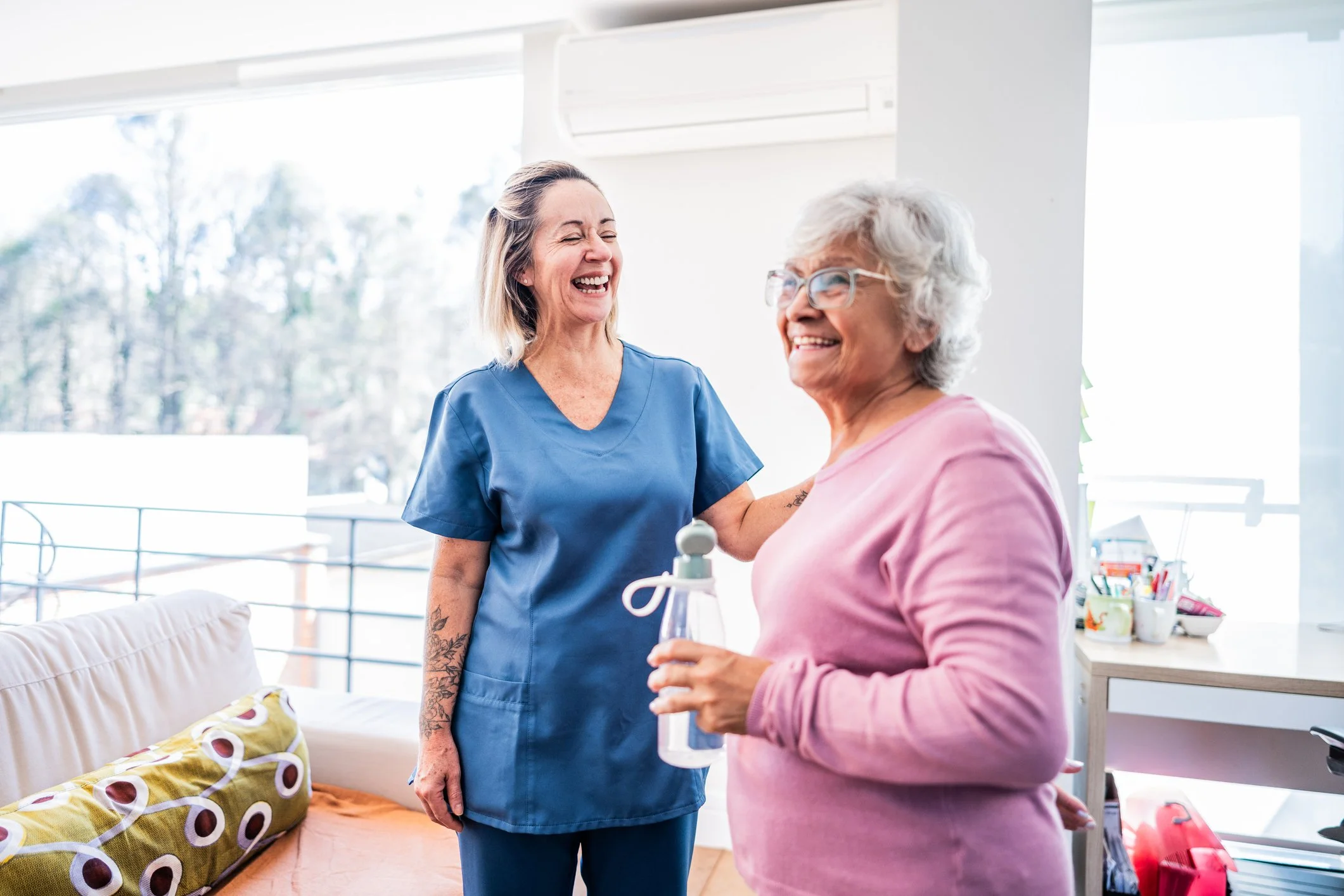 Medical professional smiling and talking with an elderly woman holding an oxygen tank in a bright room.