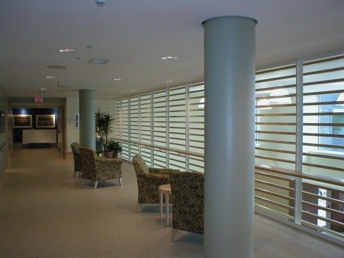 Interior of a modern building with large windows, seating area with patterned armchairs, side table, and potted plant.