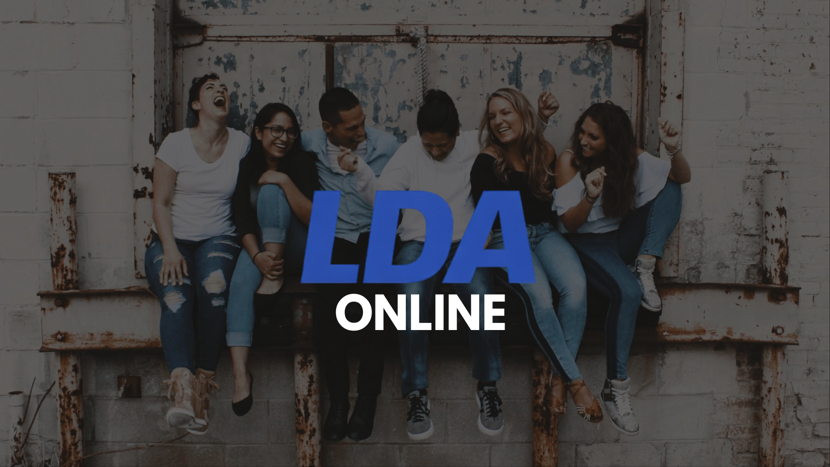 Group of six young adults sitting on a rusty metal ledge against a distressed wall, laughing and celebrating. Overlaid text reads 'LDA ONLINE' in large blue and white letters.