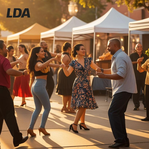 People dancing and socializing outdoors at a festive event with white tents in the background during sunset.