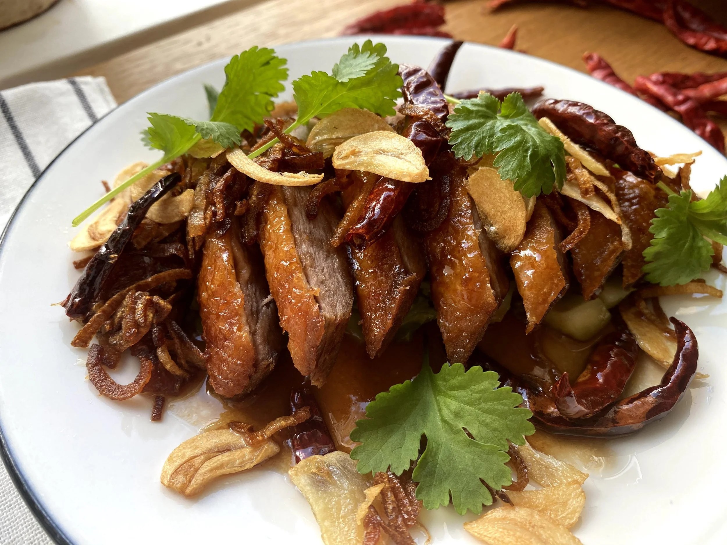 Plated traditional Chinese crispy duck with herbs and garlic slices.
