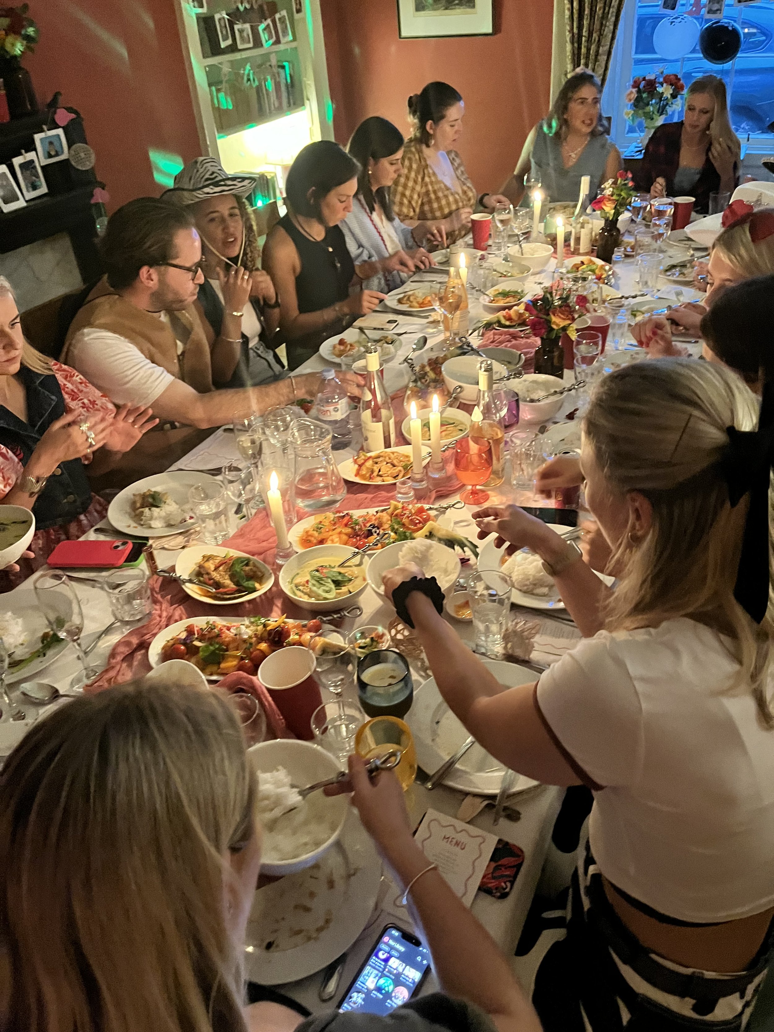 A large group of people gathered around a banquet table enjoying a meal at a celebration dinner in a warmly lit room with decorative lights and flowers.