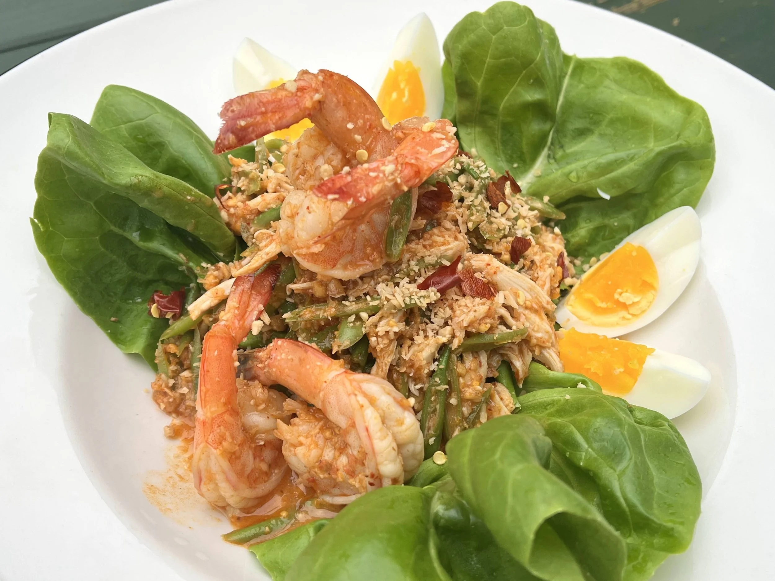 Salad with cooked shrimp, boiled eggs, green lettuce, and chopped nuts on a white plate.