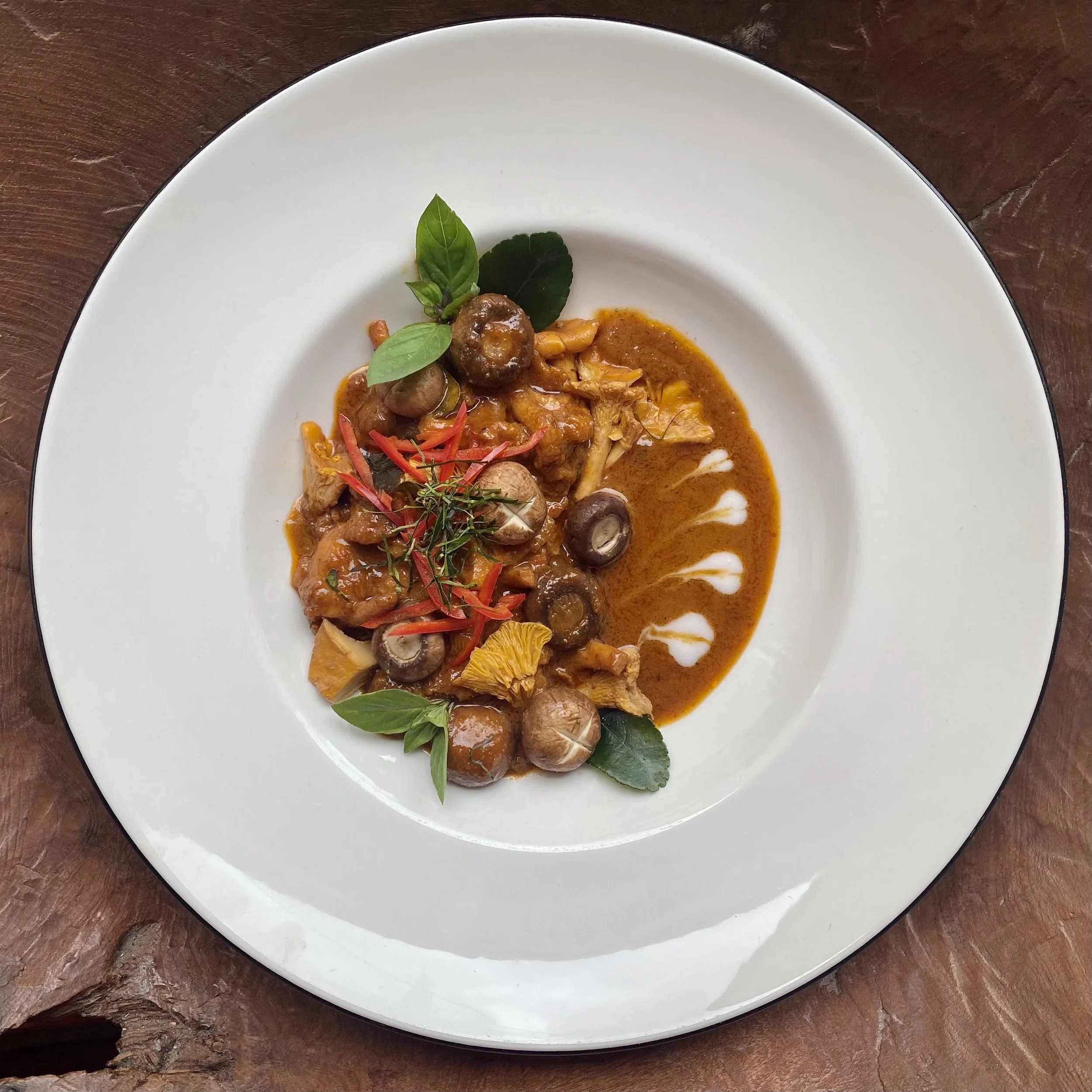 A plated dish featuring a sauce with mushrooms, herbs, and vegetables, garnished with fresh green leaves and red herbs on a white plate.