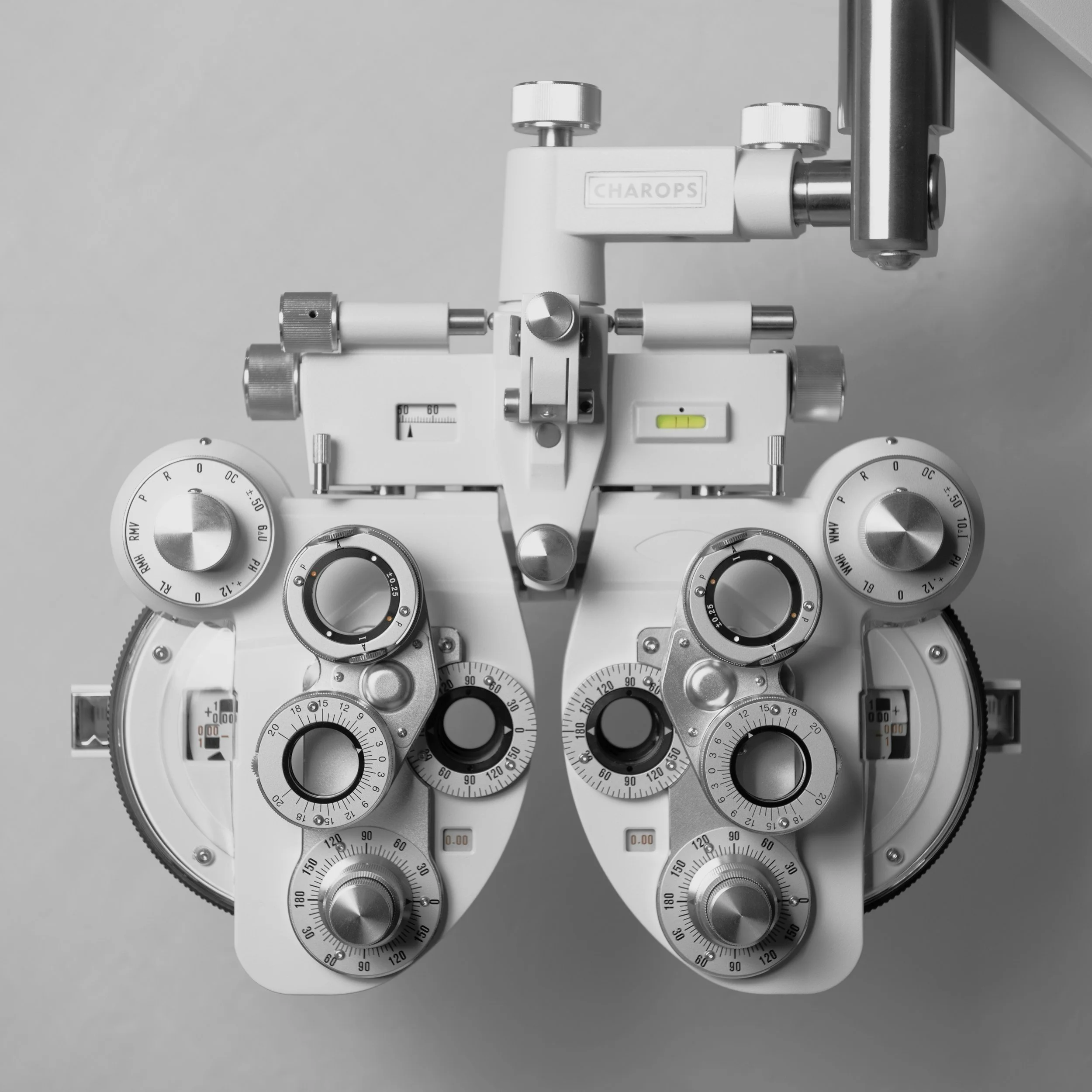 A white ophthalmic phoropter with multiple dials and adjustment knobs, used for eye examinations, placed against a plain background.