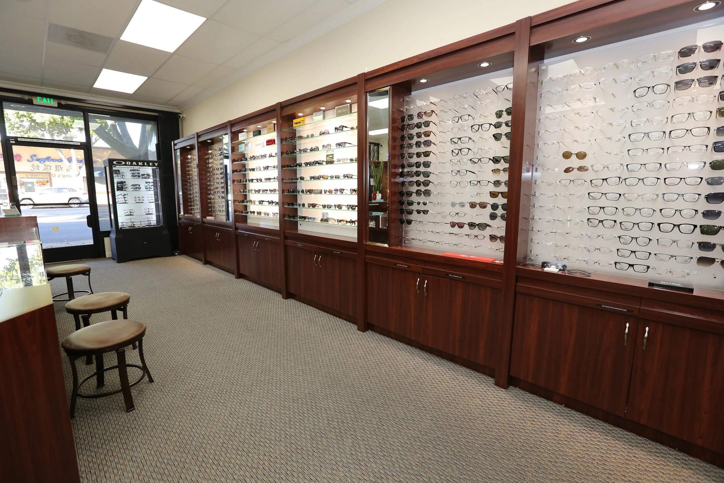 Interior of an optometrist store with display cases full of eyeglasses and sunglasses, and a door with a window showing outside view.