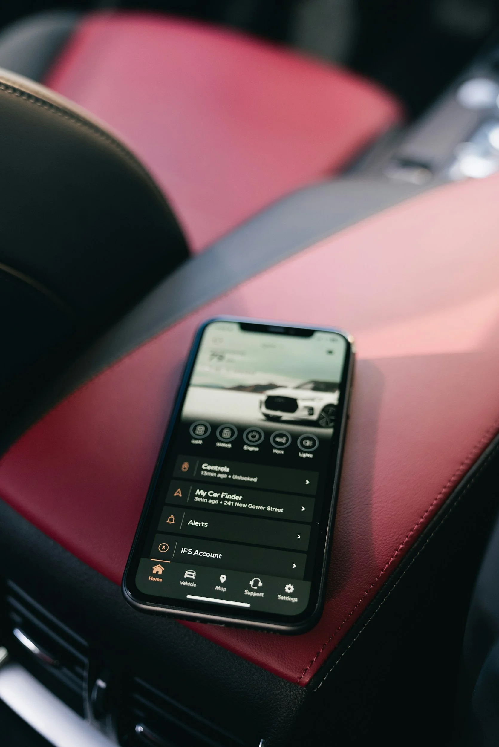 Smartphone displaying a car control app resting on a pink surface inside a vehicle.