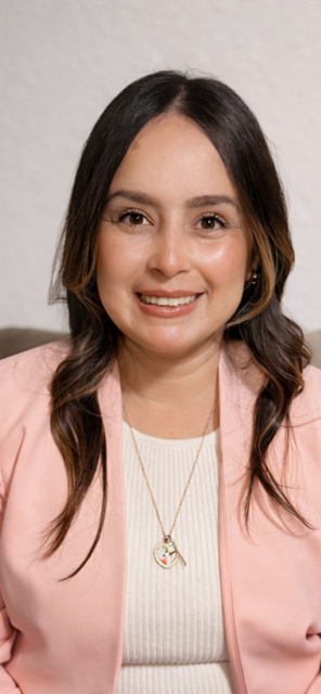 A young woman with long dark hair wearing a pink blazer, white top, and a gold necklace, smiling at the camera.