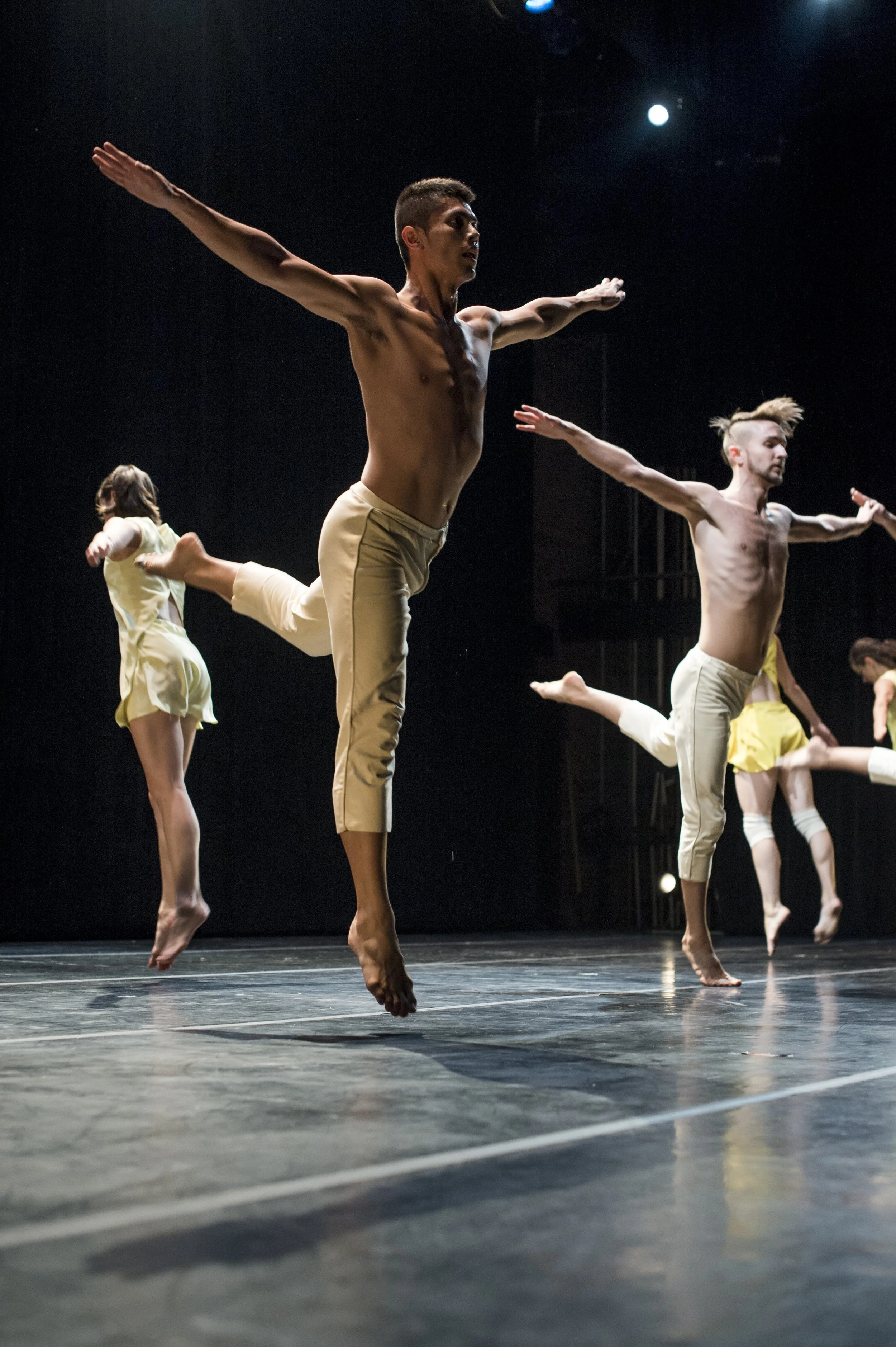 Dancers performing on stage with arms extended and mid-air jumps during a dance performance.