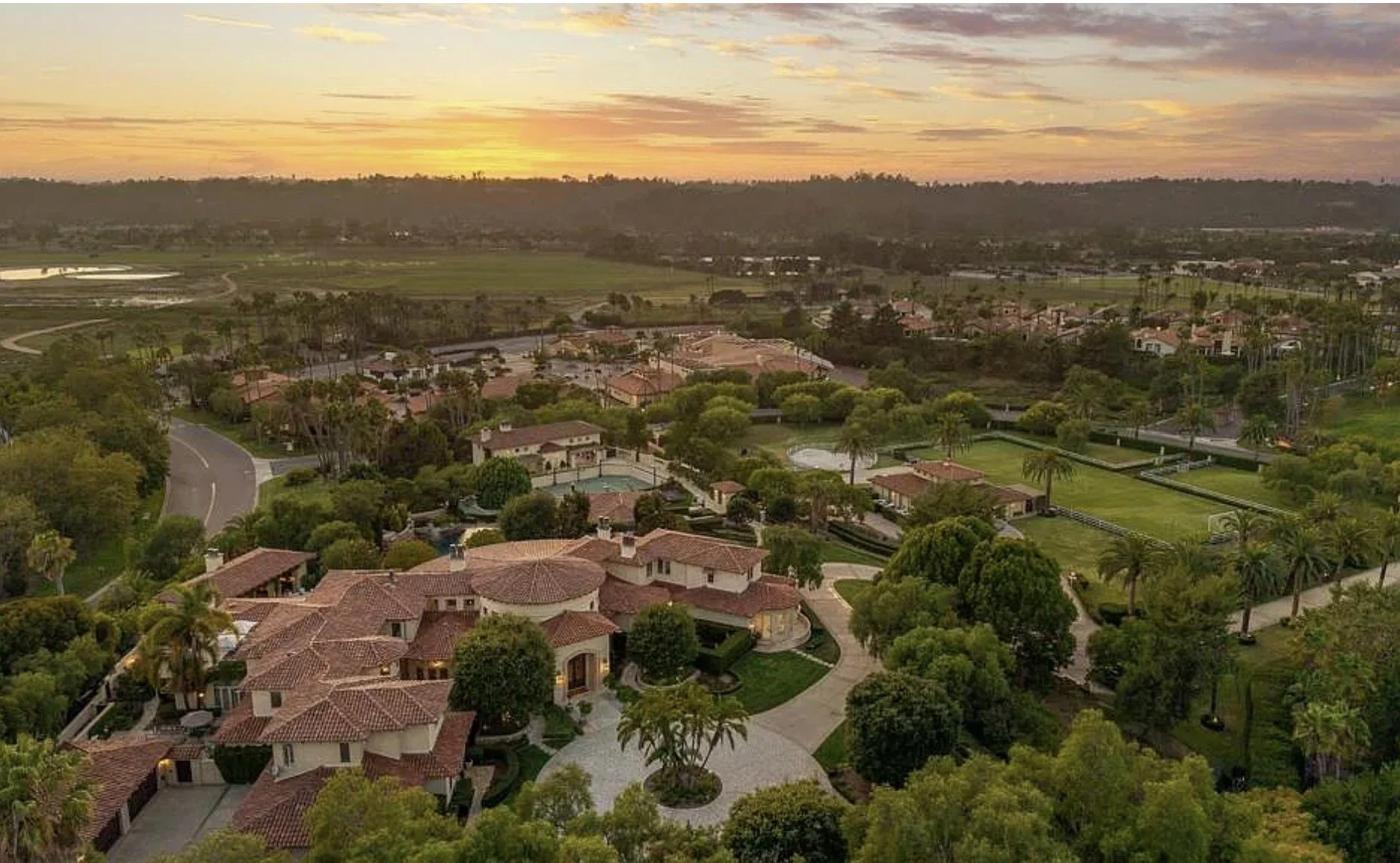 Aerial view of a suburban neighborhood at sunset with houses, trees, and a golf course.