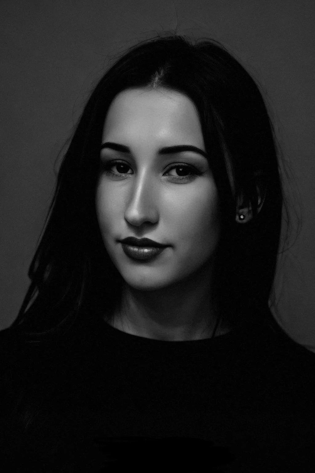 A black-and-white portrait of Agatha Frisch, a co-founder of Megagatha, with long dark hair, wearing earrings and dark lipstick, looking directly at the camera with a subtle smile.