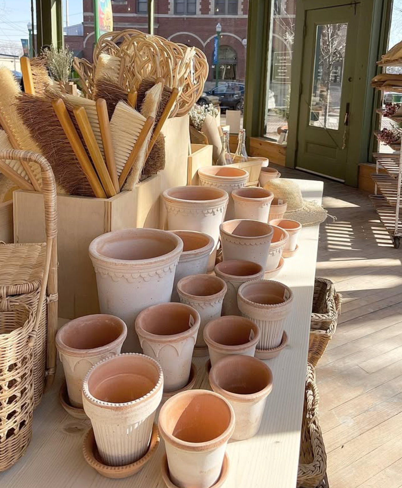 Display of empty terracotta flower pots and gardening tools inside a sunlit shop.