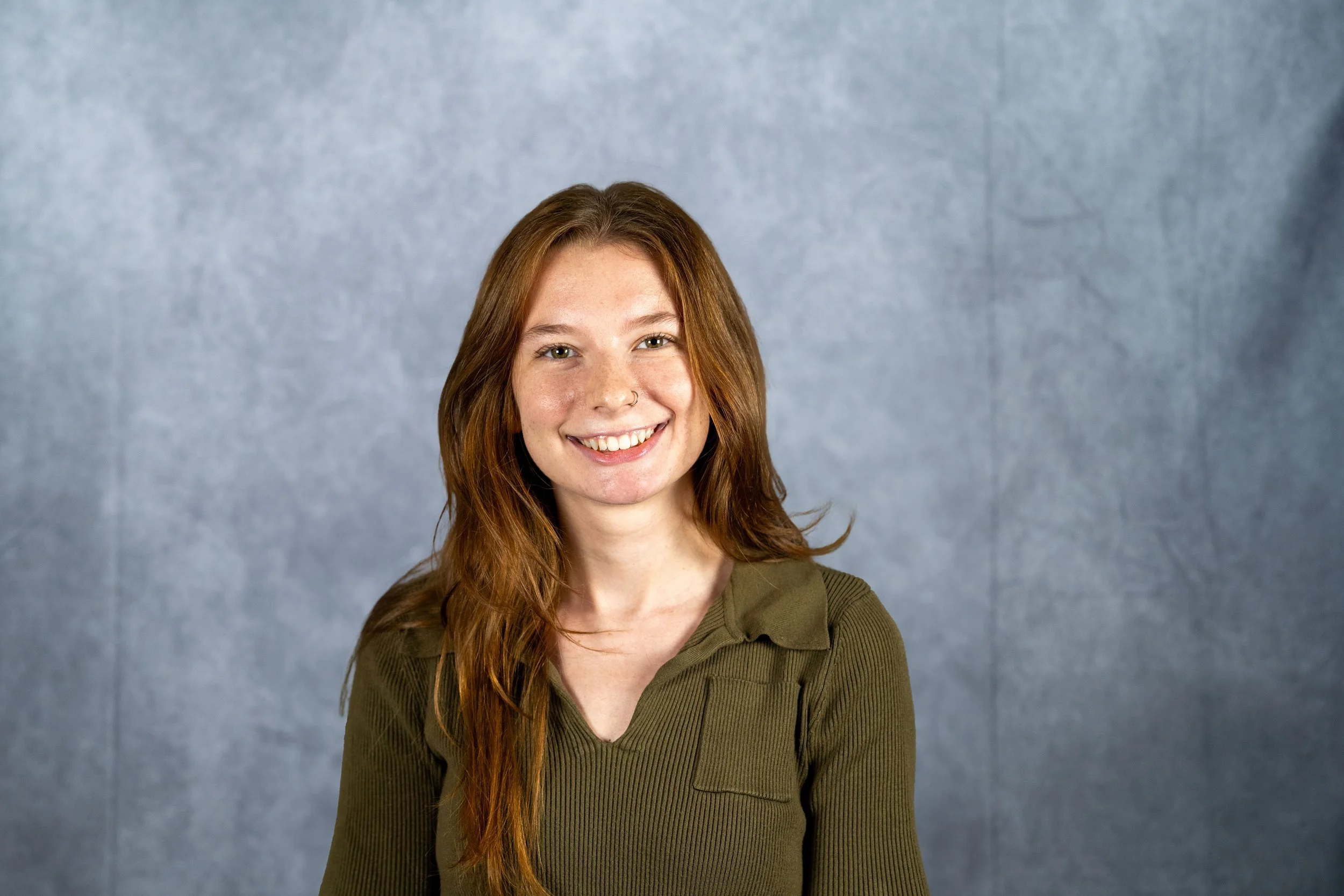 A person with brown hair smiling in front of a blue blackground