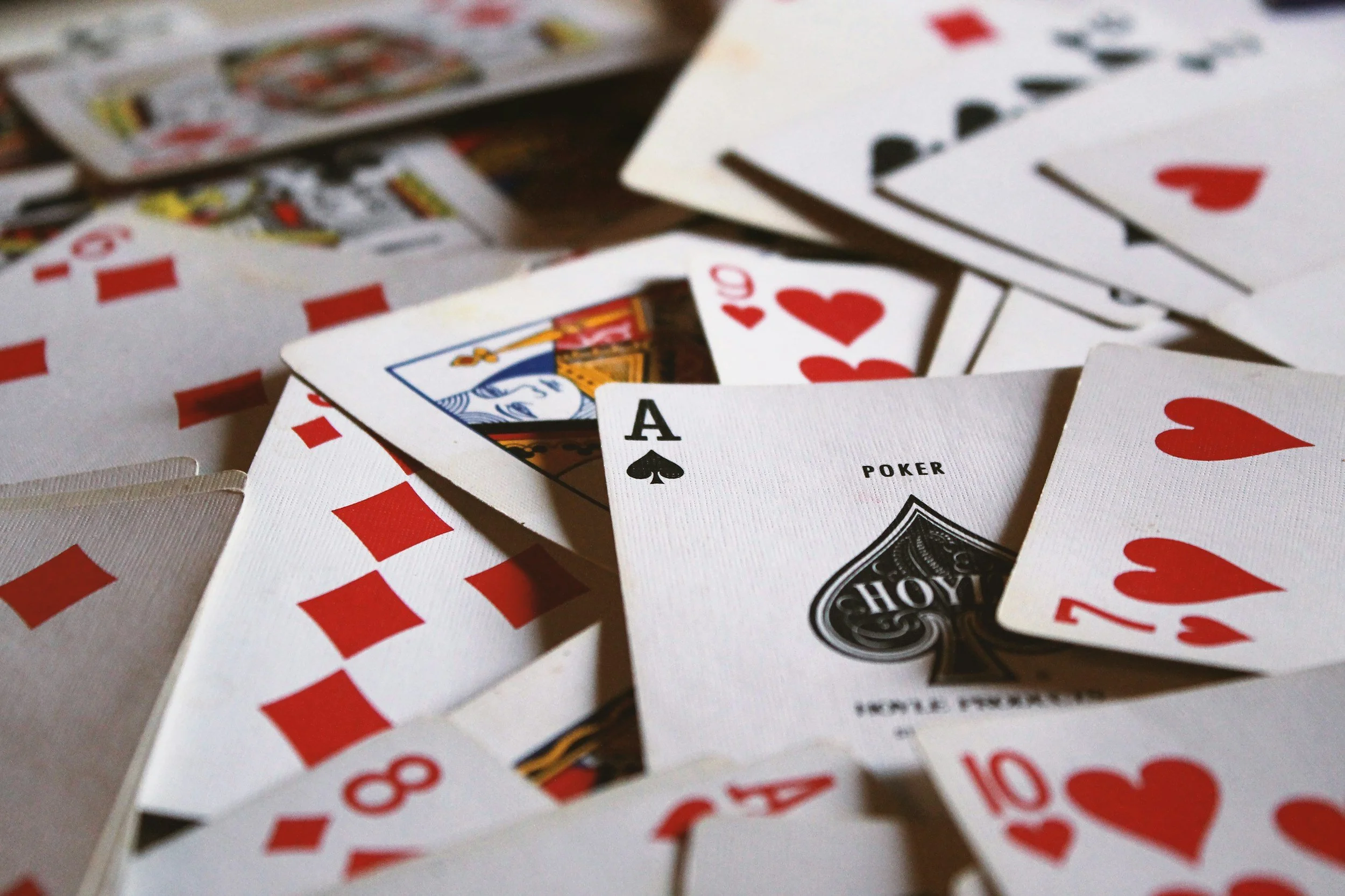 Close-up of scattered playing cards, including an Ace of Spades and a Queen of Hearts, on a table.