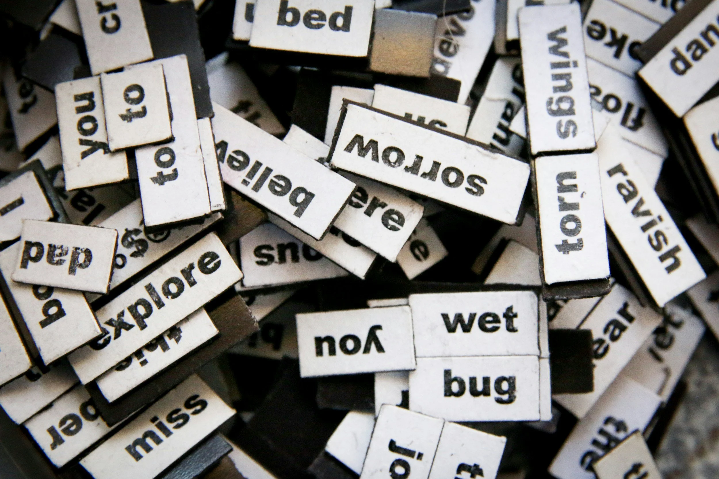 A close-up view of small white rubber stamps with black text, showing various words such as 'wet,' 'sleep,' 'more,' 'bug,' and 'explore,' scattered and overlapping.