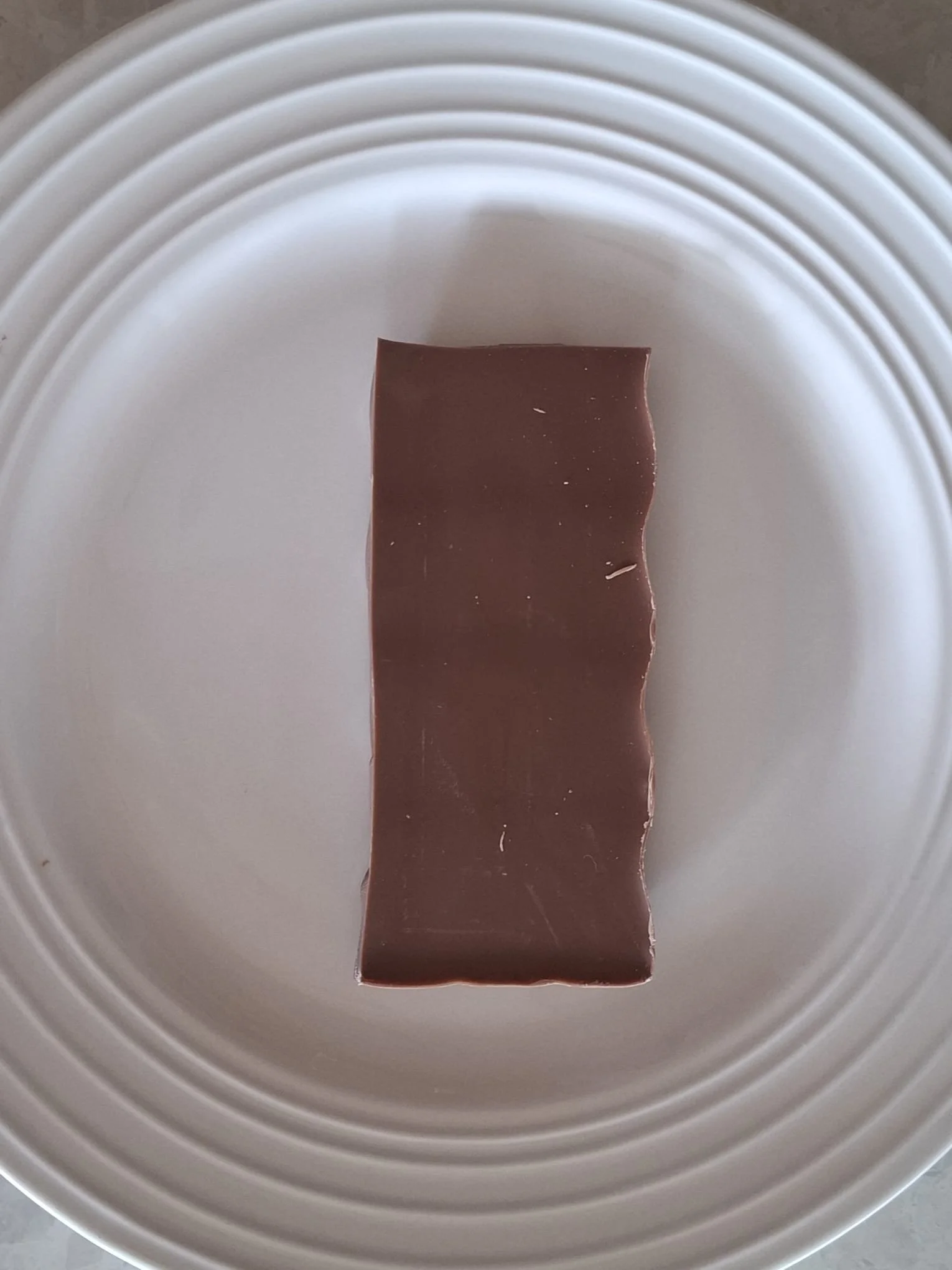 A piece of milk chocolate on a white plate with concentric ridges.