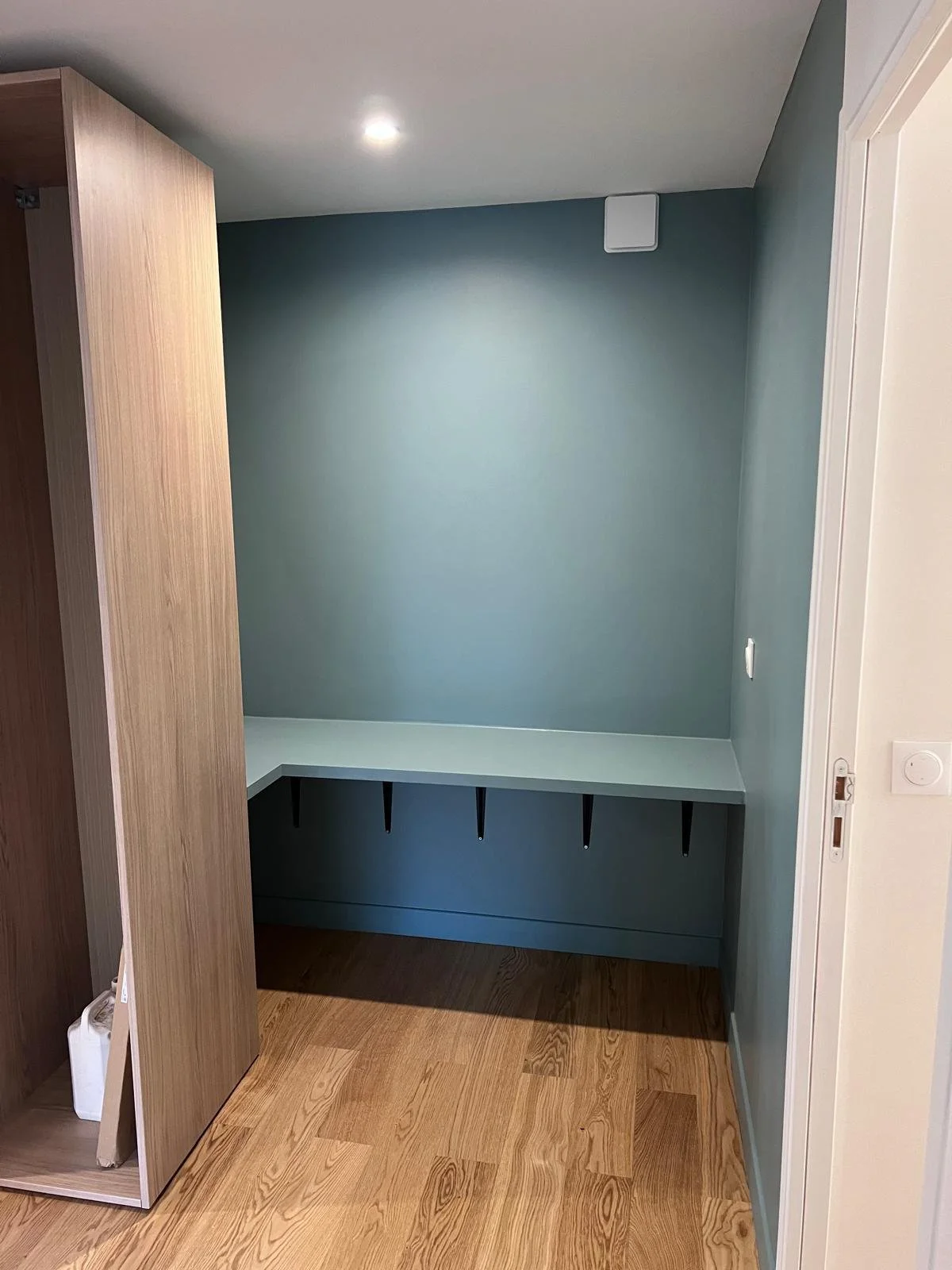 Espace intérieur avec mur gris, plan de travail bleu et étagères noires, sol en bois.
