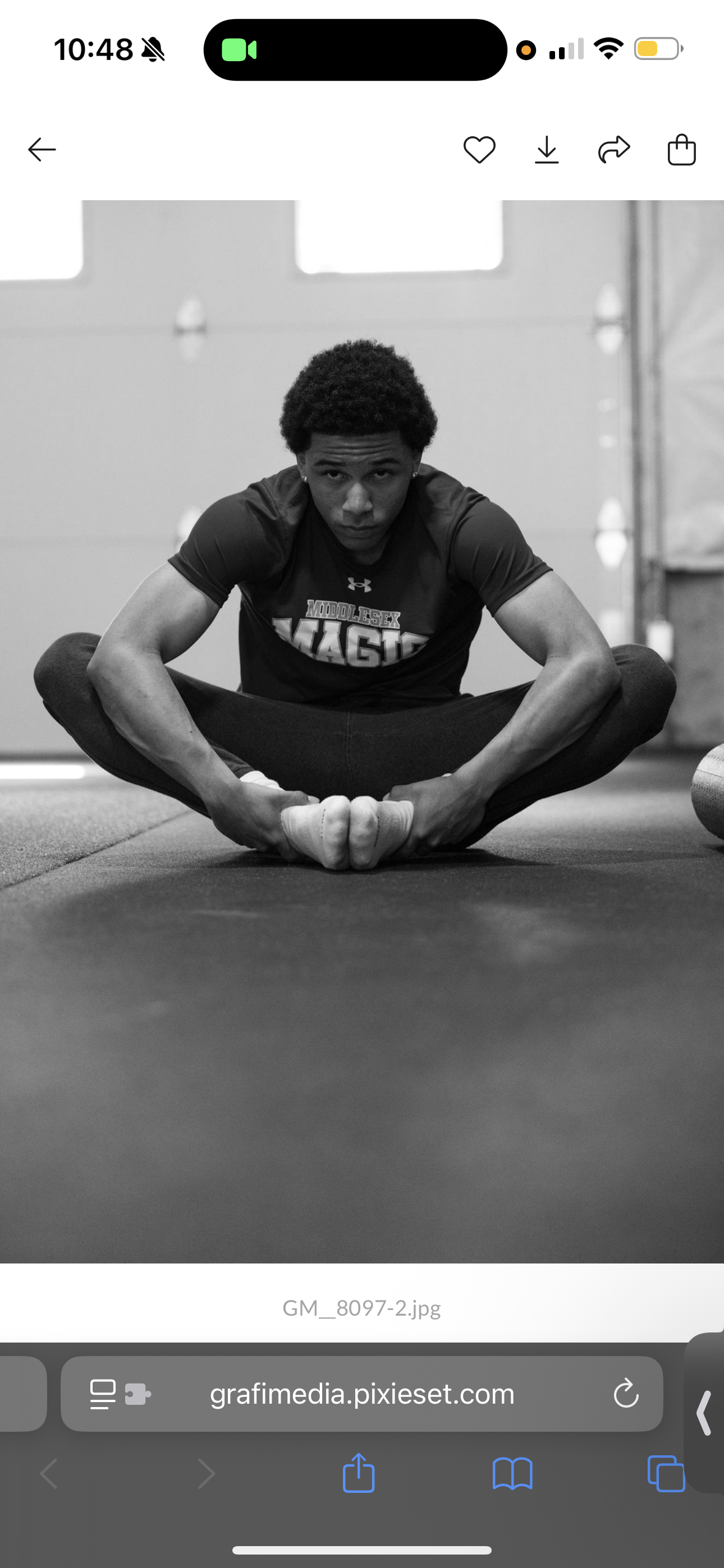 A young man with curly hair sitting cross-legged on a gym floor, looking at the camera, wearing a dark athletic shirt with the word 'Magic' on it.