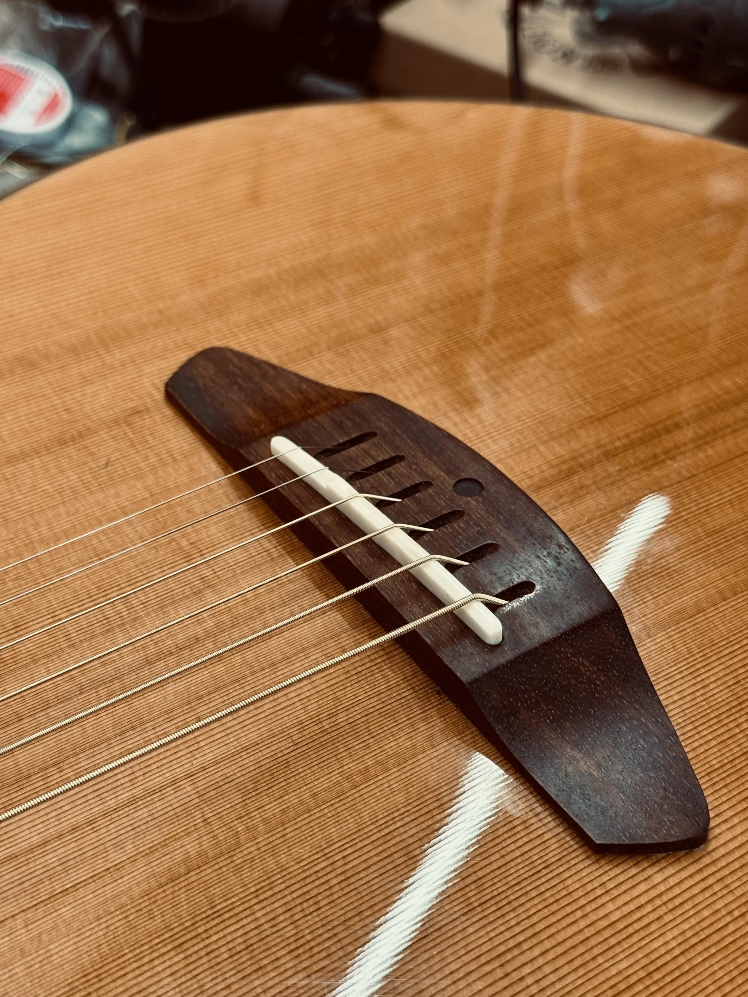 Close-up of an acoustic guitar bridge, strings, and saddle on a wooden body.