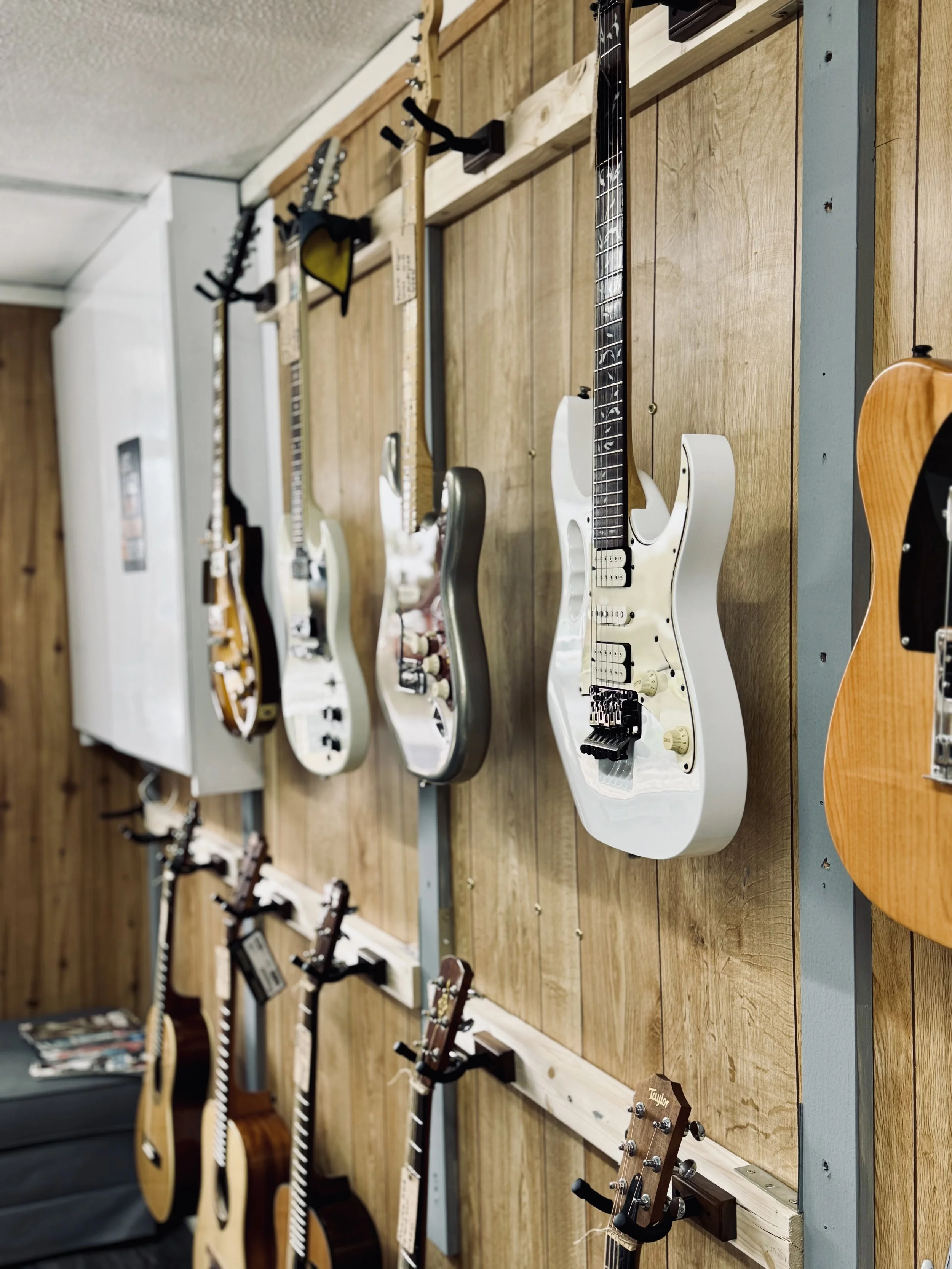 A display of electric and acoustic guitars hanging on a wooden wall at a music store.