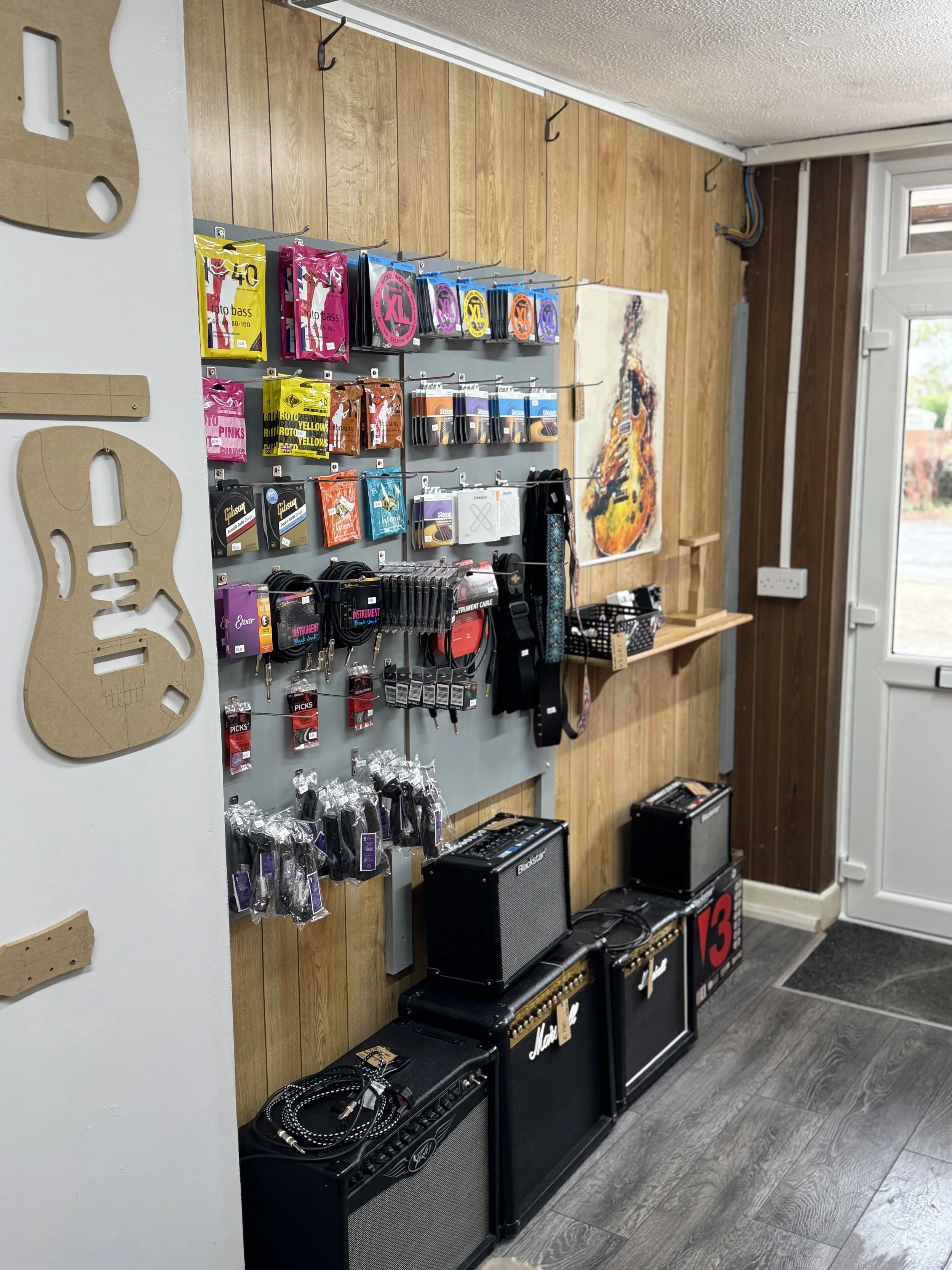 Guitar accessories display with strings, straps, and cables in a music store.
