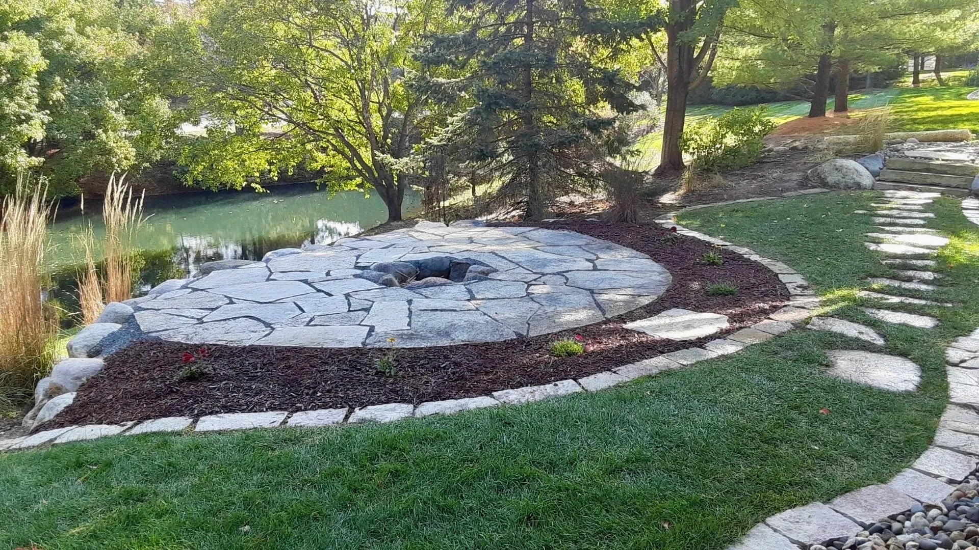 A landscaped backyard with a stone pathway, a small pond, and trees providing shade.