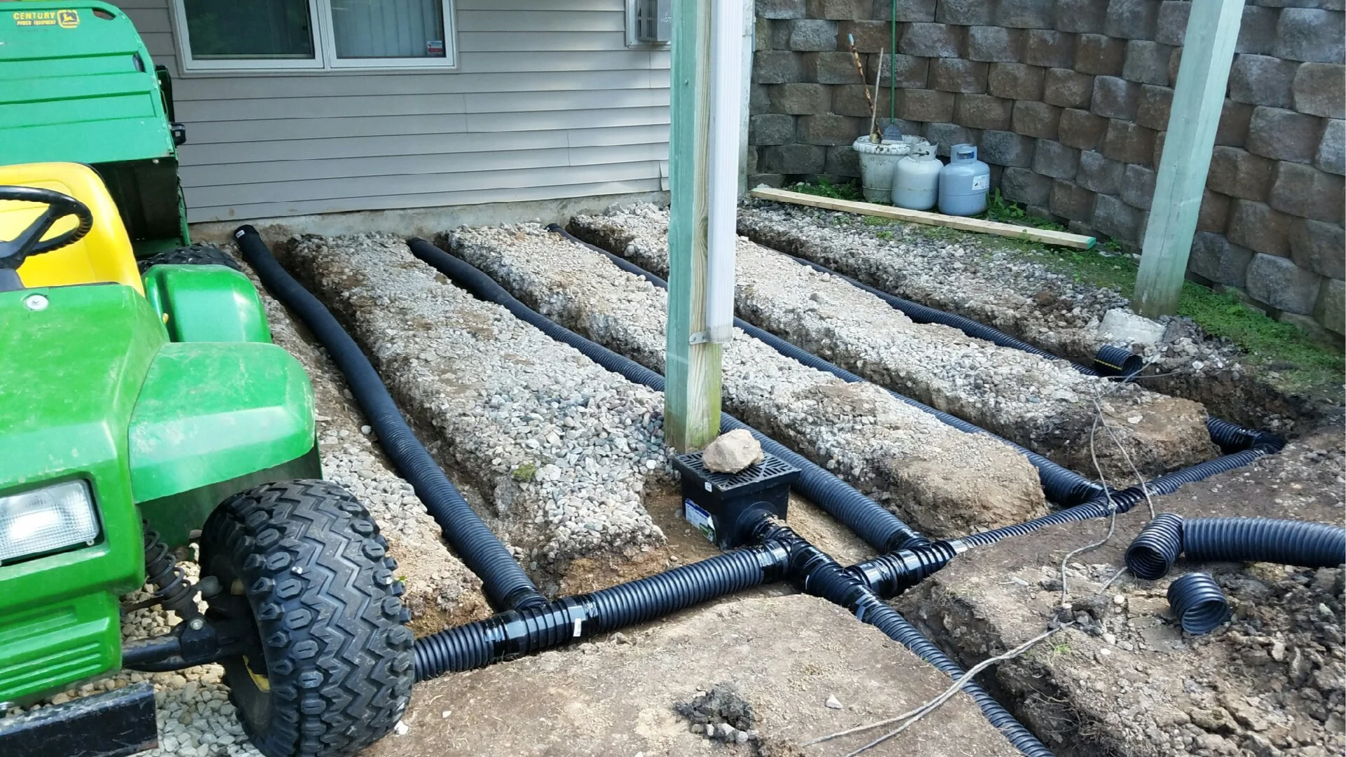 Underground piping installation with black corrugated pipes in trenches next to a house.