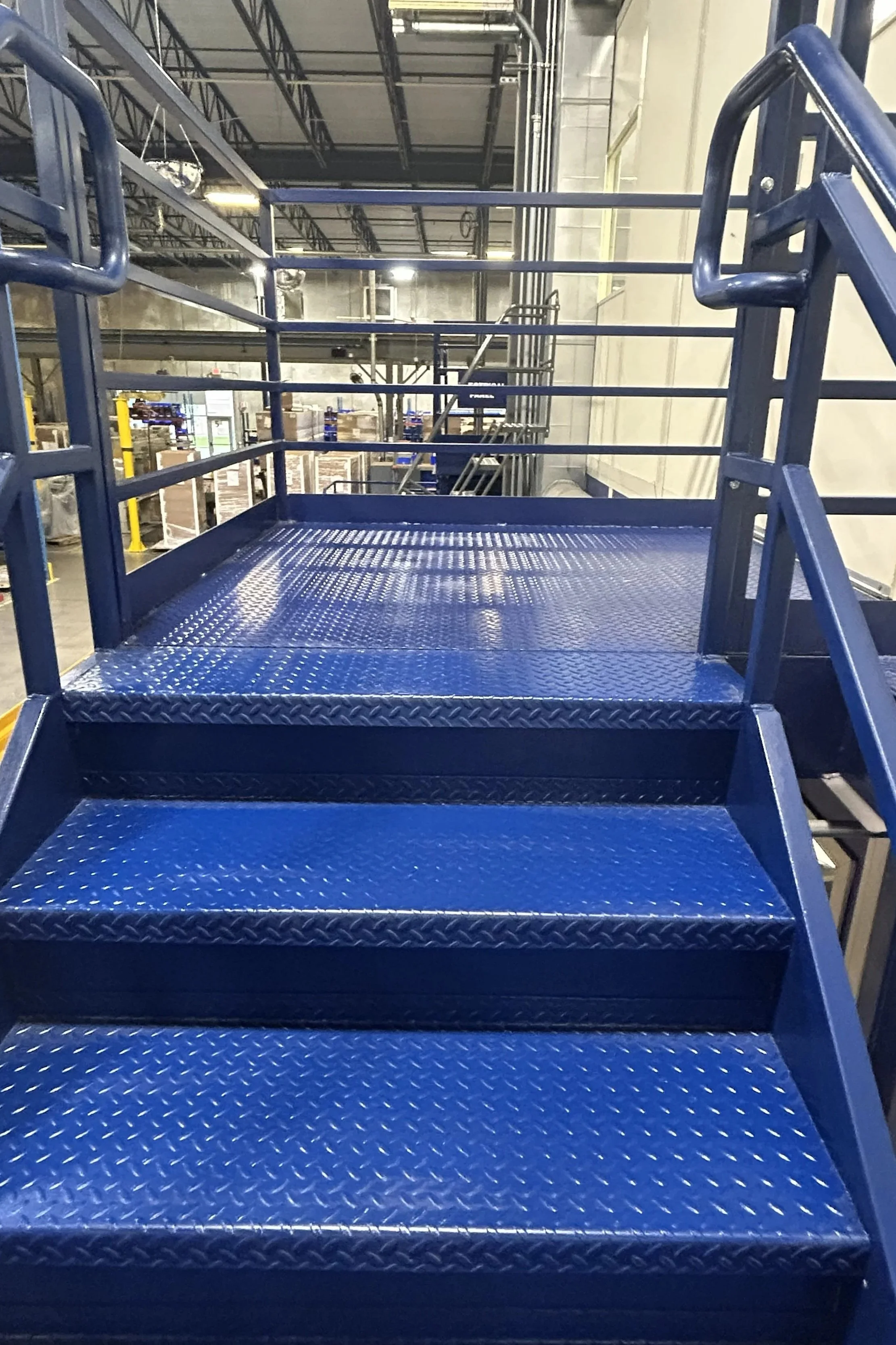 Blue industrial staircase with metal steps and guardrails inside a warehouse.