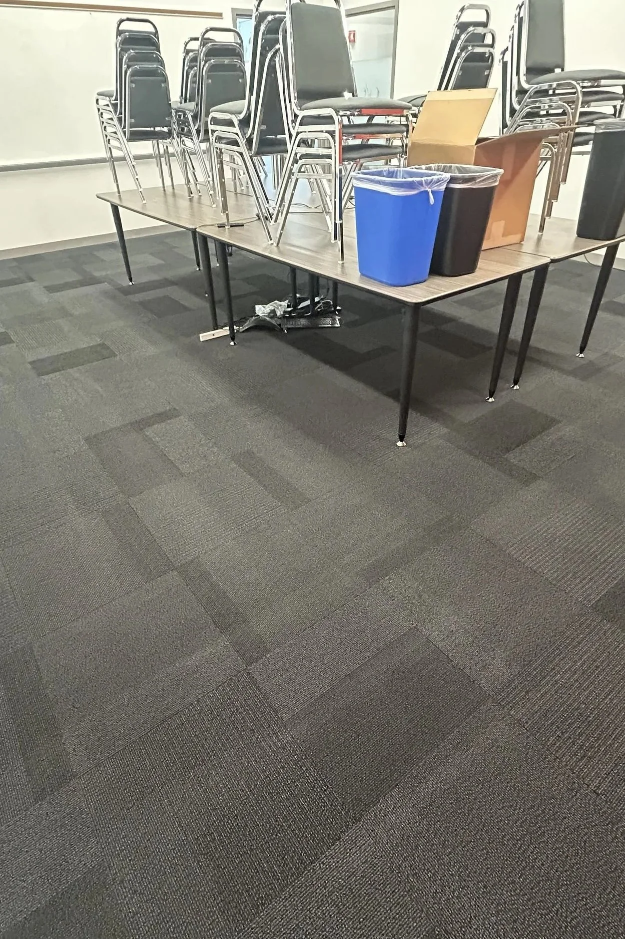 A table with stacked chairs on top, trash cans, and boxes in a room.