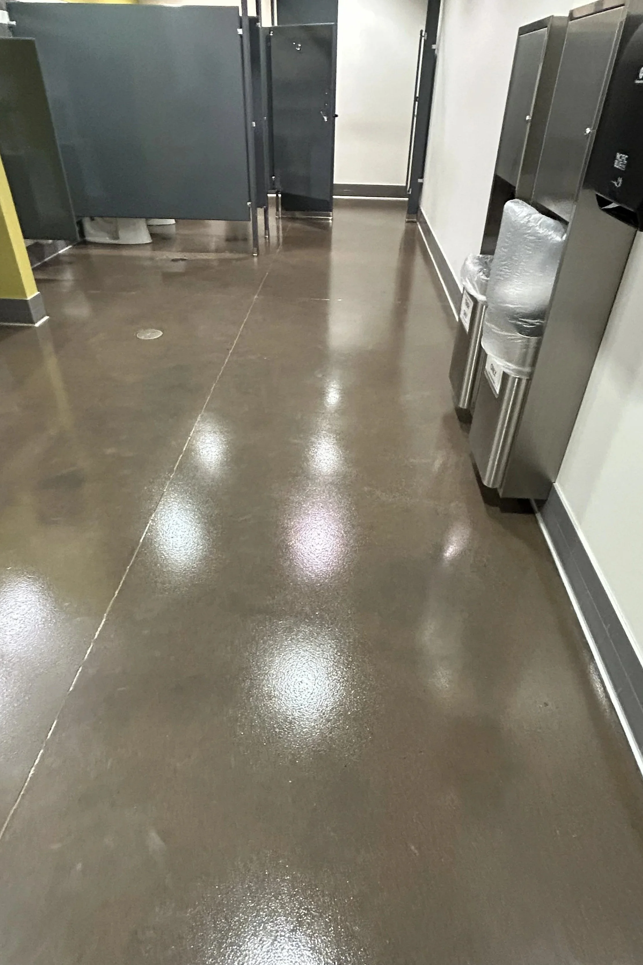 A polished concrete floor with a water fountain on the right and bathroom stalls in the background.