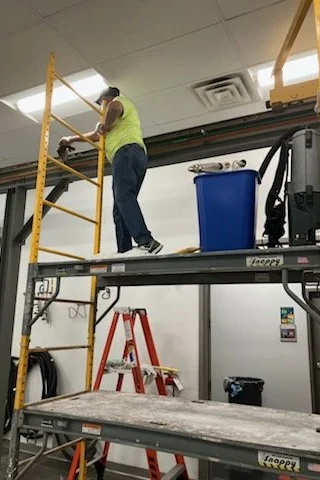 A worker on a yellow scaffold working on the ceiling of an industrial or commercial space.