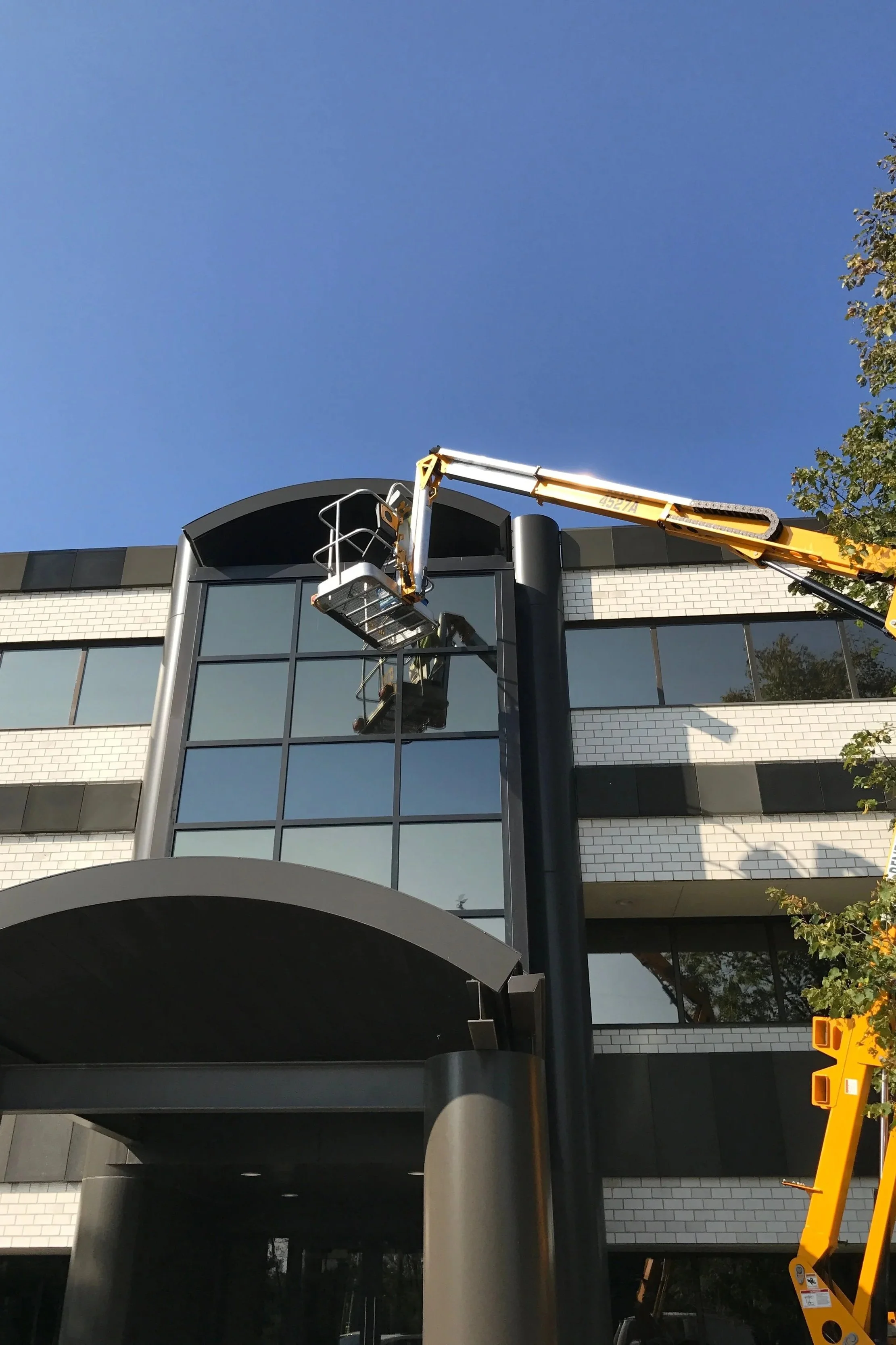 Construction workers installing glass windows on a modern building using a crane lift.