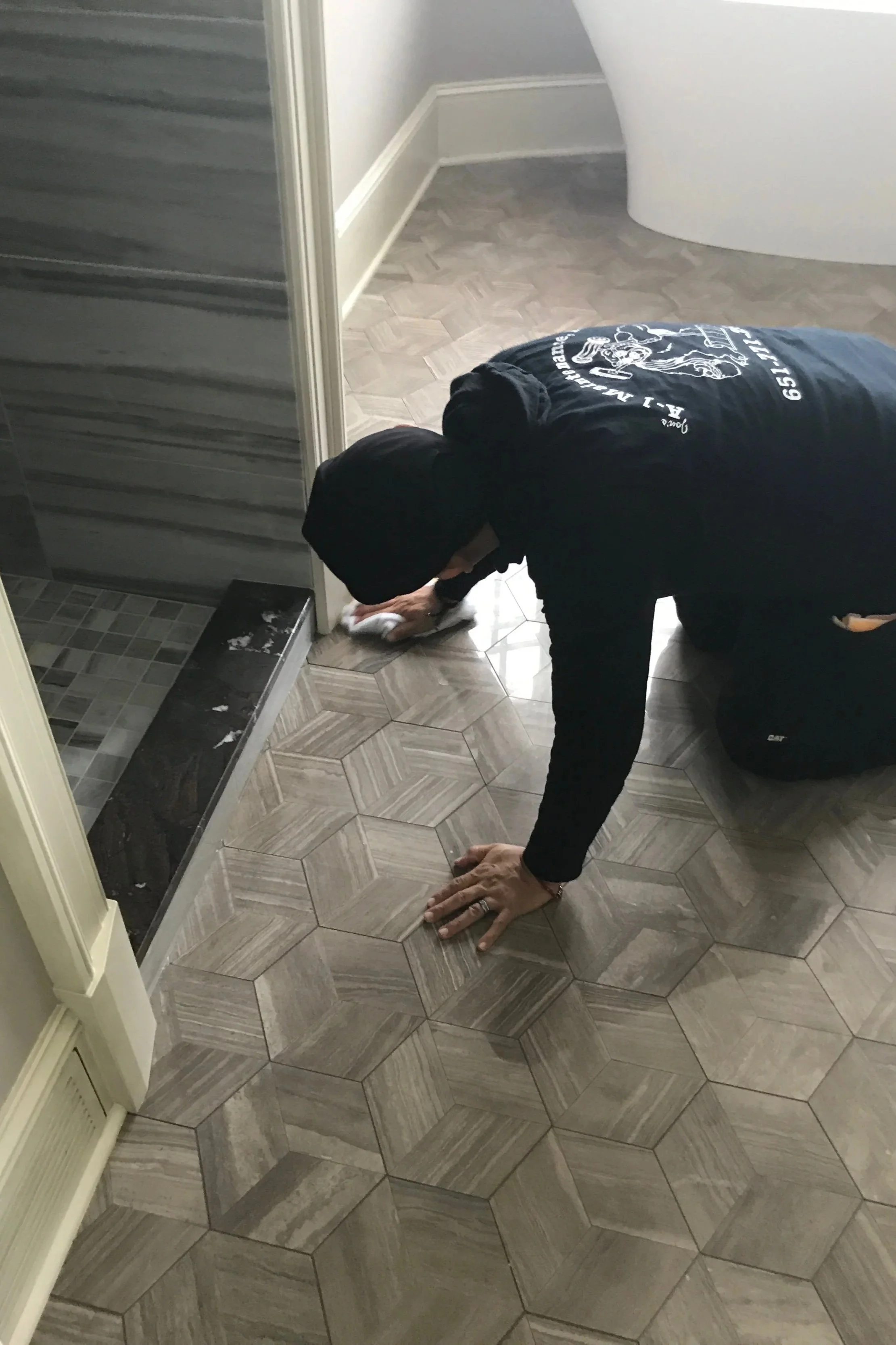 Person cleaning the floor with a cloth in a room with hexagon patterned tiles.
