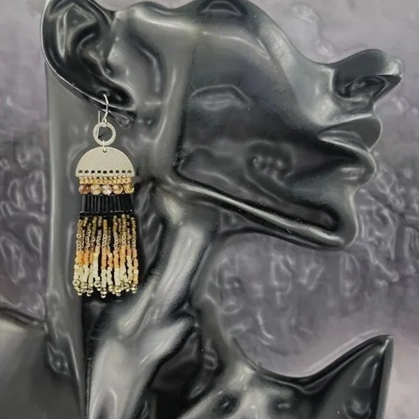 A black mannequin head displaying a large, ornate earring with a silver hoop, a semi-circular silver piece with dotted pattern, and hanging beads in black, beige, and gold colors.