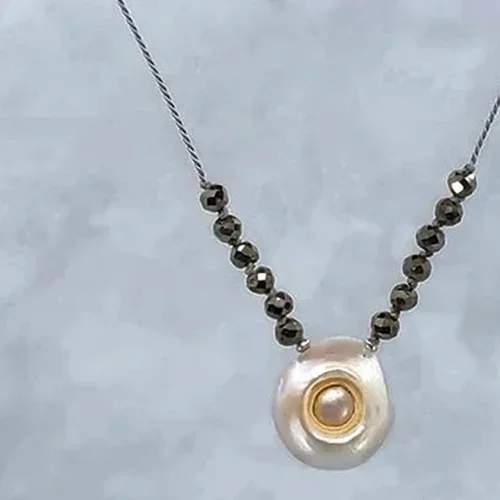 Pendant necklace with a large pearl and gold ring, adorned with small dark beads on a silver chain.