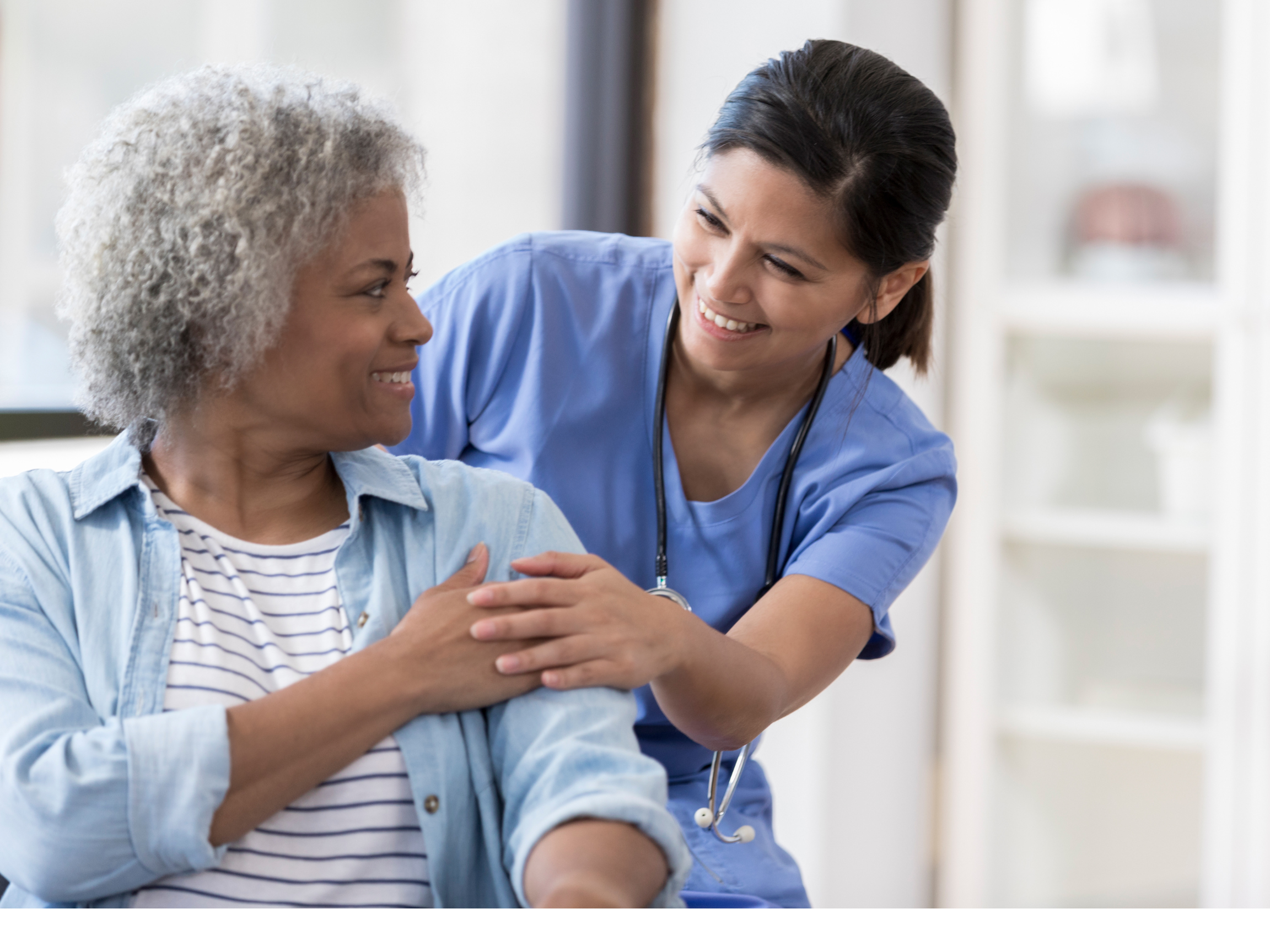 A healthcare professional smiling at an elderly woman in a medical setting.