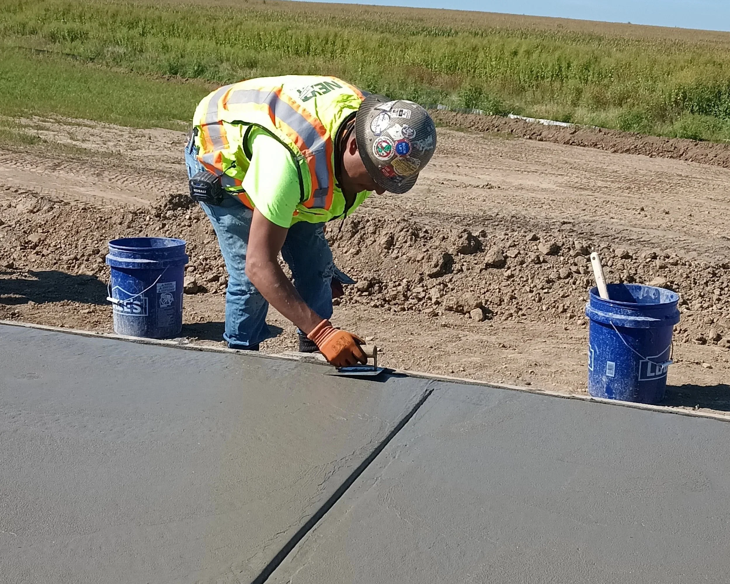 Worker in a safety vest and helmet smoothing wet concrete on a new sidewalk or road.