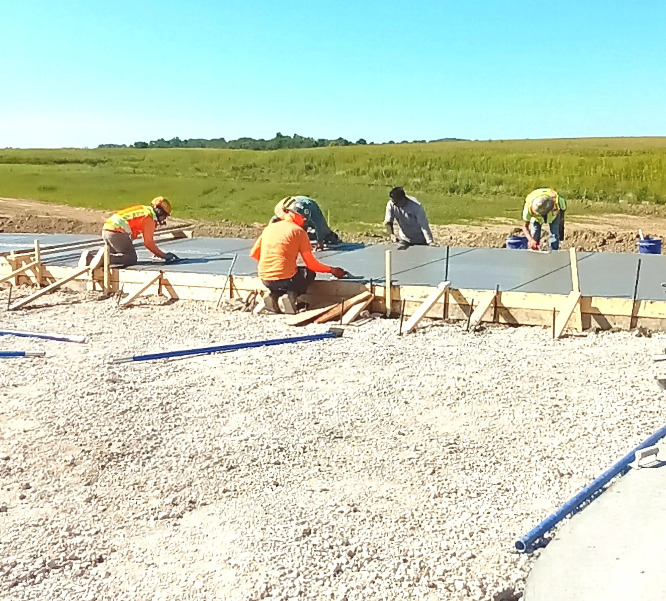 Construction workers pouring concrete on a foundation outdoors under a clear blue sky.
