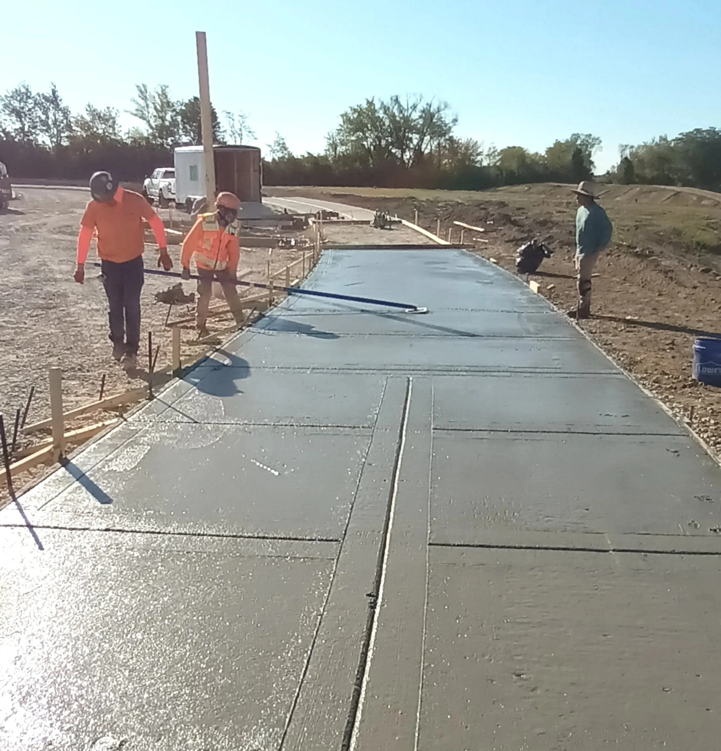 Construction workers pouring and smoothing concrete on a sidewalk or pathway at a construction site.