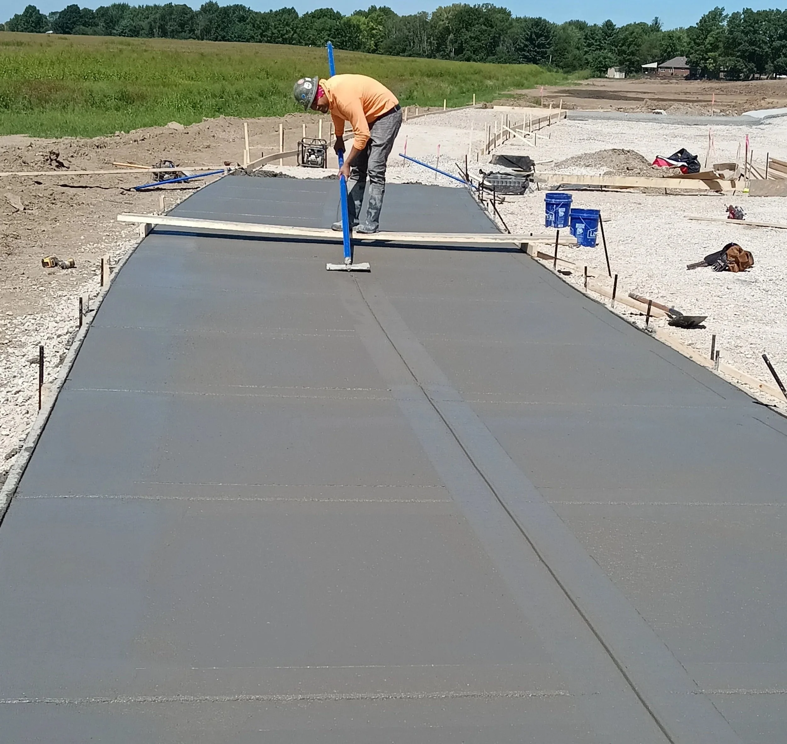 Construction worker smoothing wet concrete with a long-handled tool on a large slab of freshly poured concrete at a construction site.