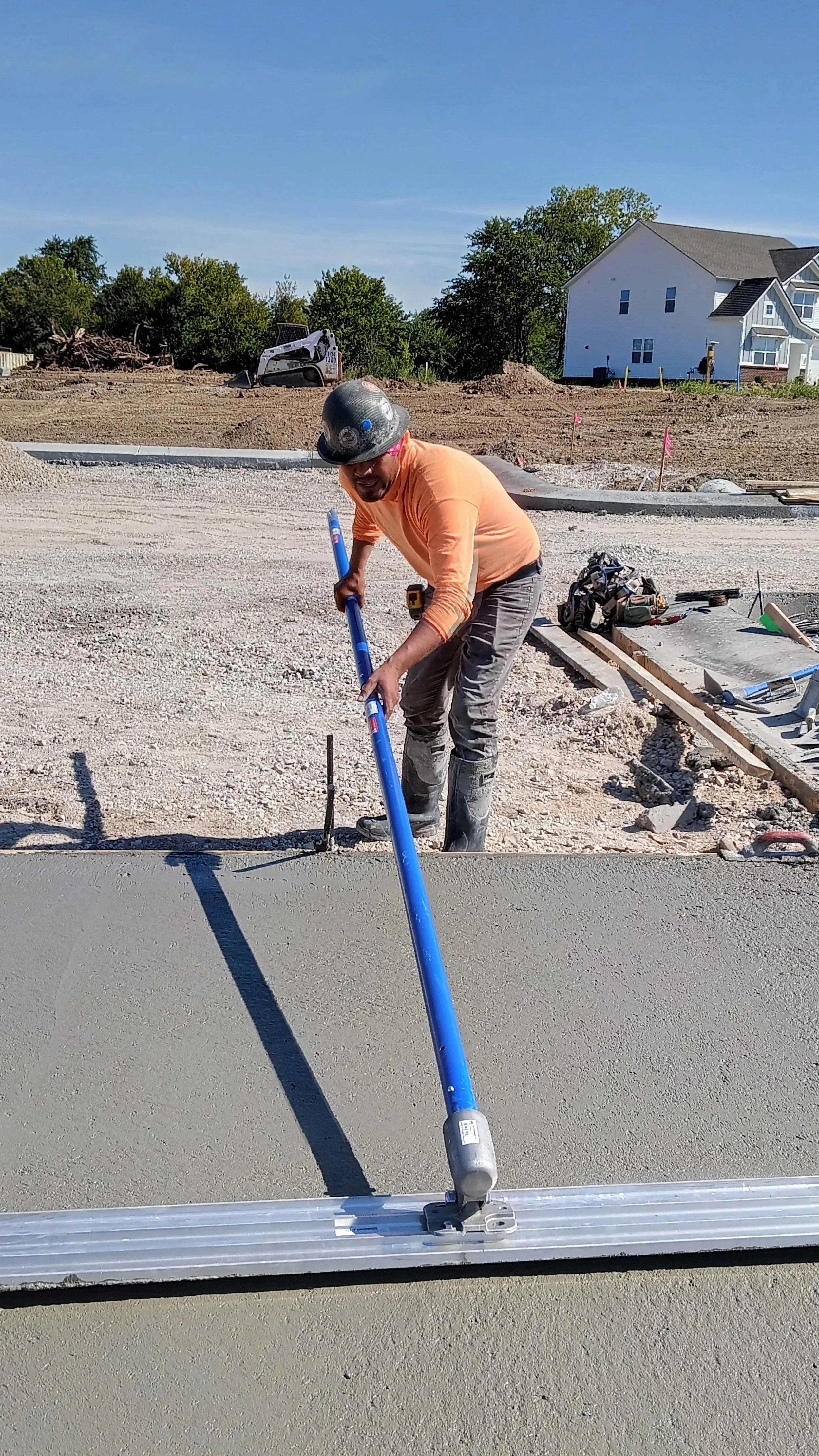Construction worker smoothing wet concrete with a long-handled tool on a new sidewalk.