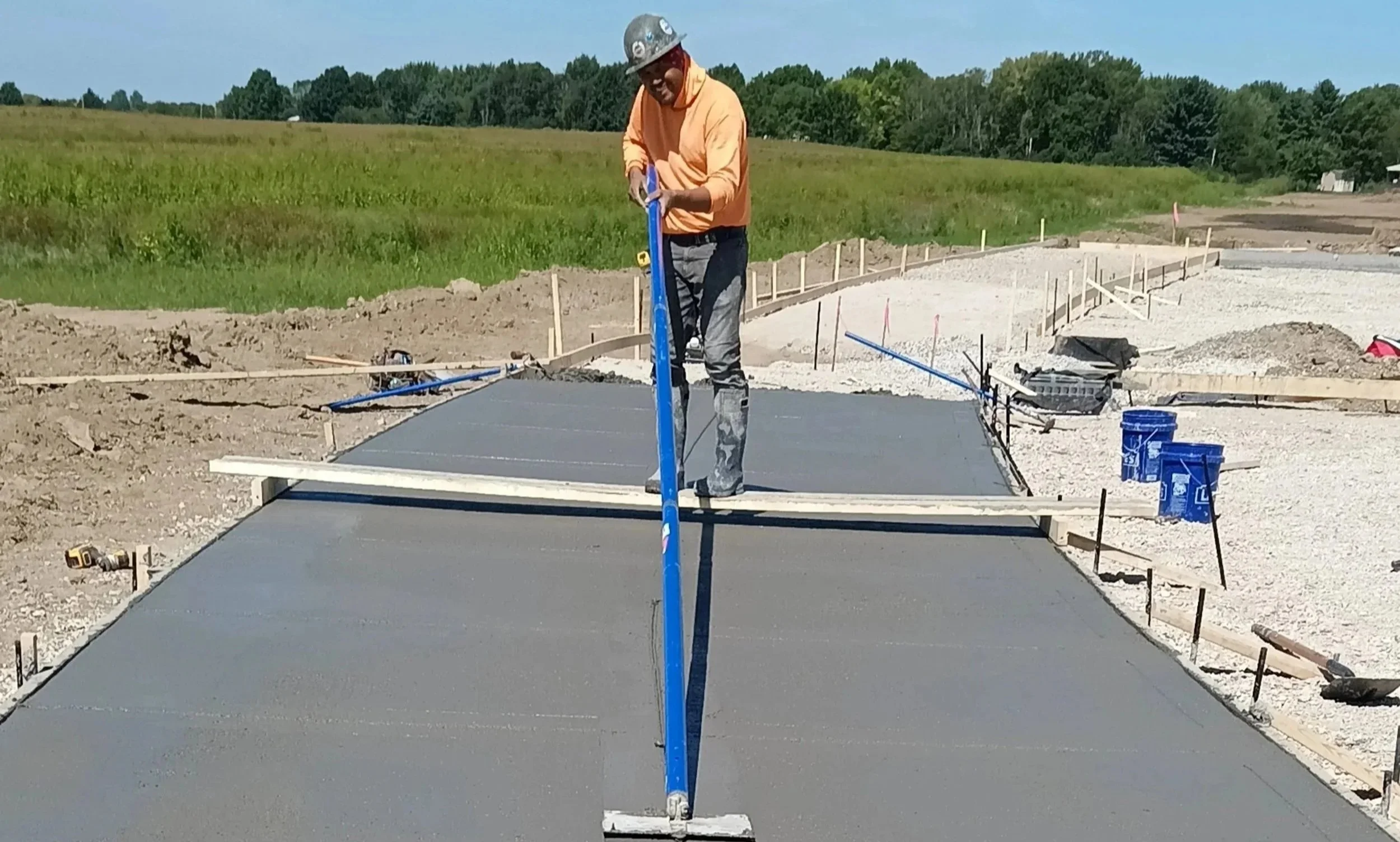 A construction worker smoothing wet concrete on a newly poured sidewalk or driveway at a construction site outdoors.
