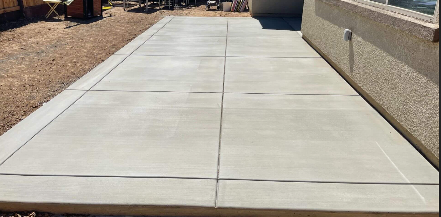 Concrete patio with large rectangular slabs adjacent to house wall with textured stucco finish
