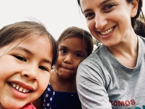 A woman and two young girls smiling outdoors.