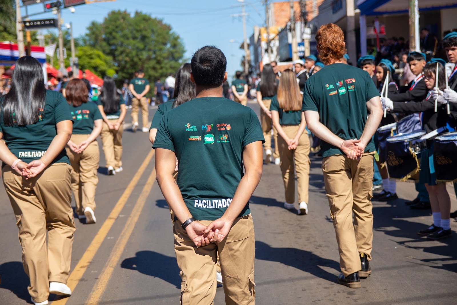 Group of students and volunteers standing in formation on a city street during a parade or event, with people and buildings in the background.