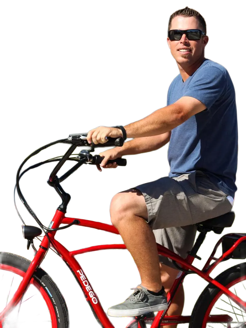 A man wearing sunglasses, a blue t-shirt, and gray shorts riding a red Pedego electric bicycle outdoors.