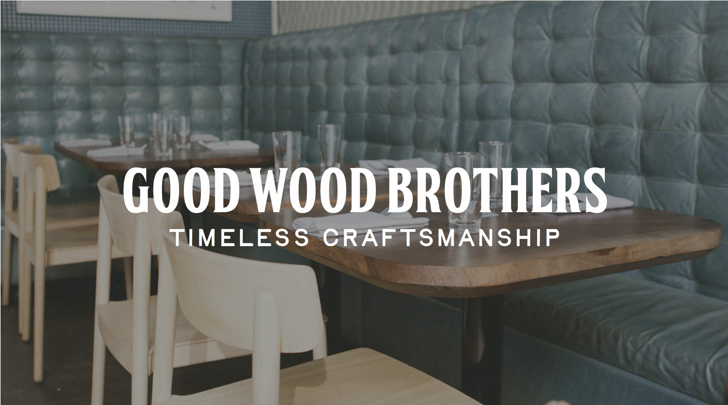 Interior view of a restaurant with a wooden table set with glasses and napkins, cushioned blue wall, and wooden chairs, with text overlay reading "Good Wood Brothers, Timeless Craftsmanship."