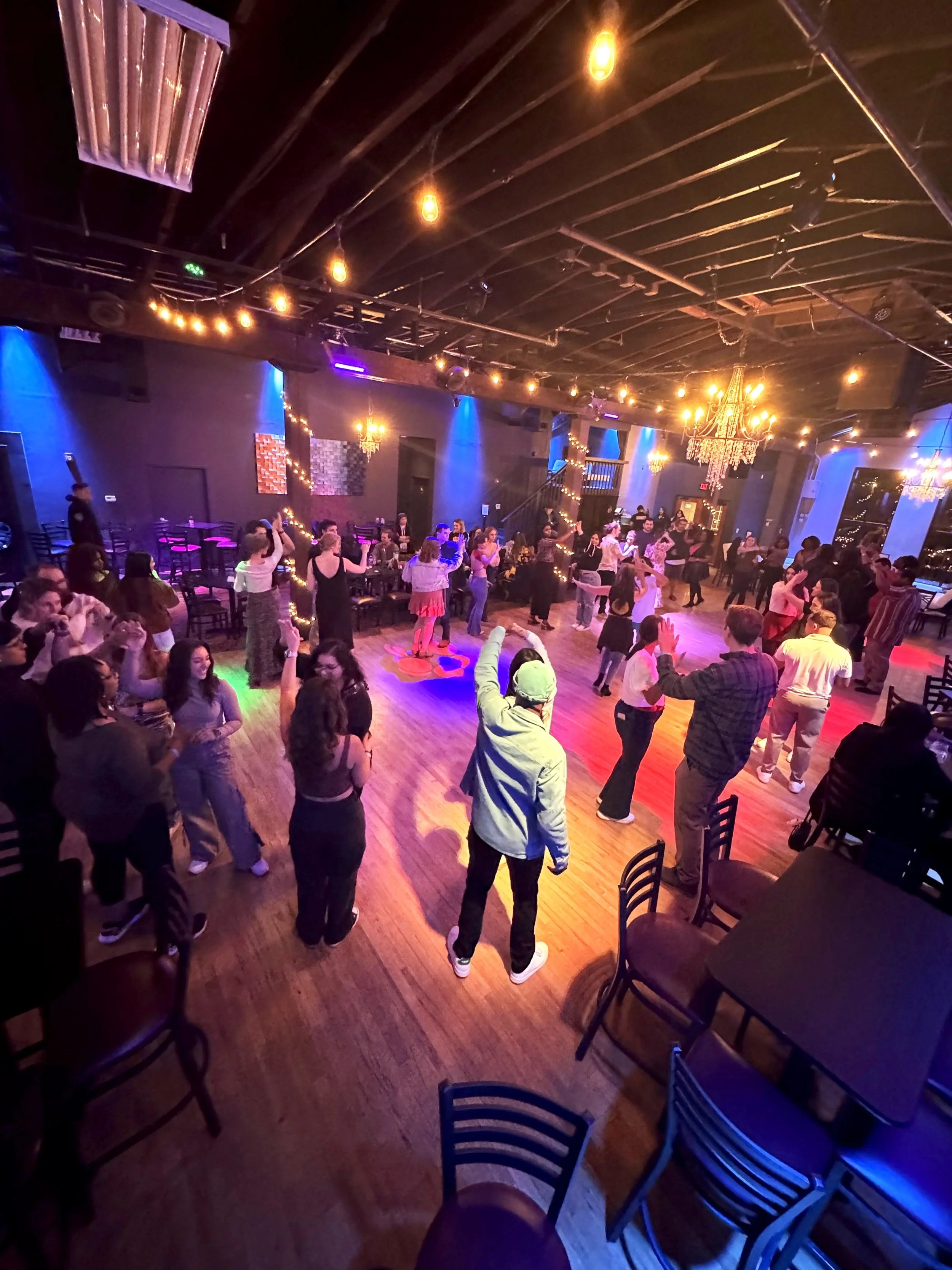 Group of people dancing at Twenty Seven event venue. The venue has string lights and chandeliers