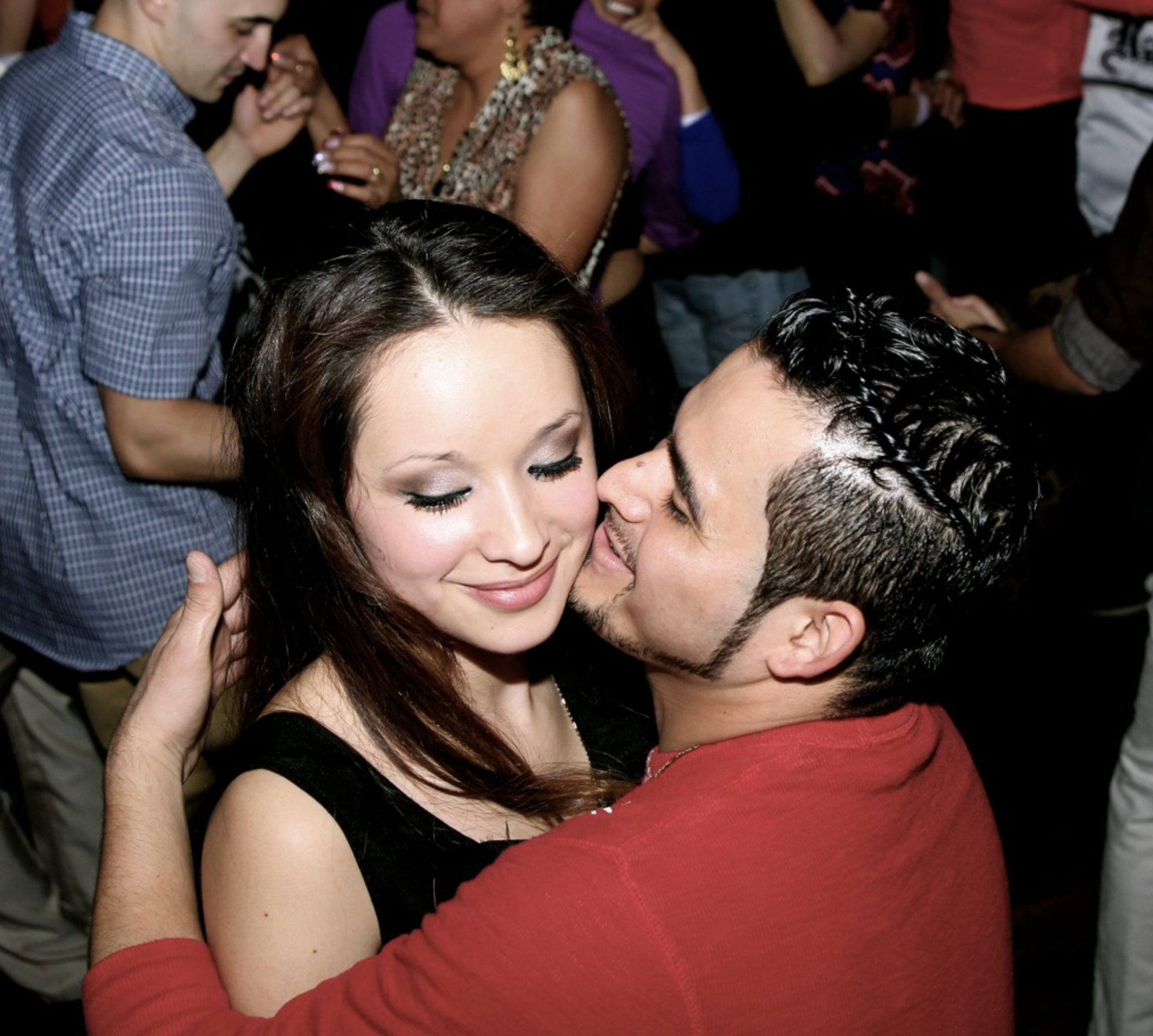 Couple dancing at a party at Twenty Seven Event venue , man embraces woman, smiling, with people dancing in the background.