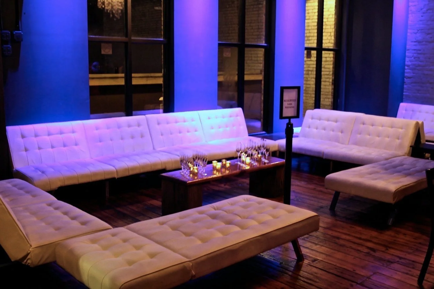 Stylish lounge with white cushioned seating, blue lighting, wooden floor, and a table with glasses and candles at Twenty Seven Venue in Little Rock Arkansas